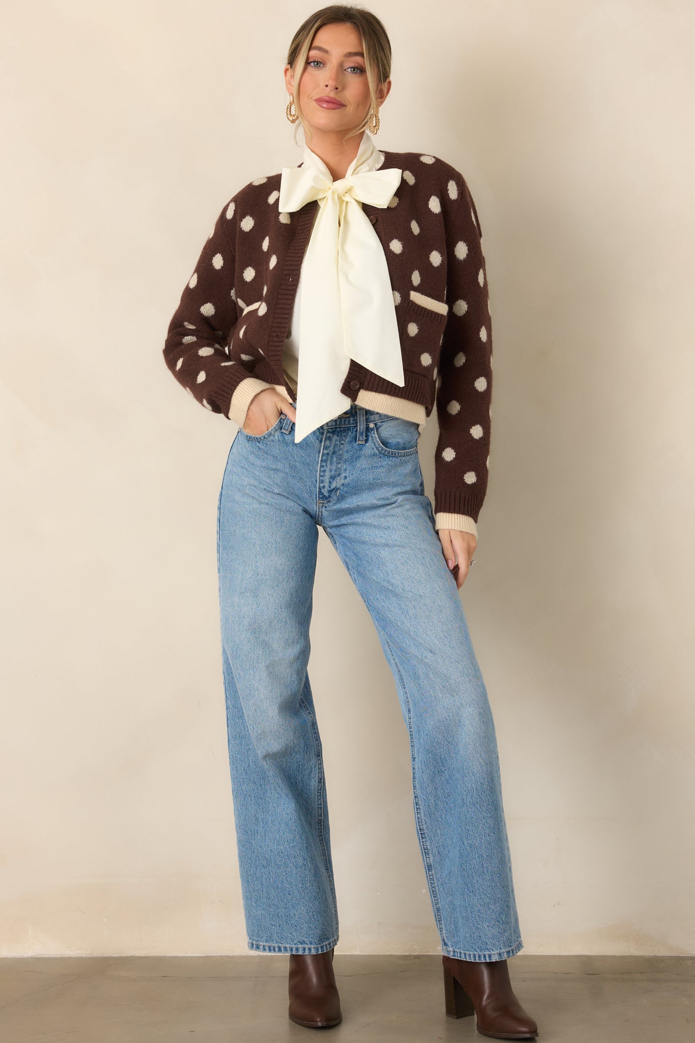 Soft brown knit cardigan covered in ivory polka dots, featuring a crew neckline, button front, patch pockets, and contrasting ivory trim.