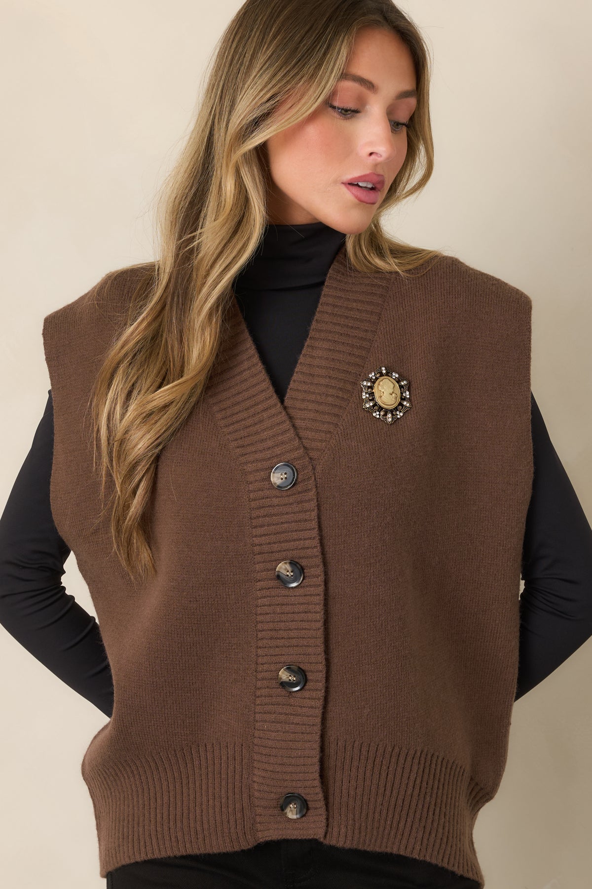 Brown knit vest highlighting the deep V-neckline and wide ribbed trim framing the neckline and button placket.
