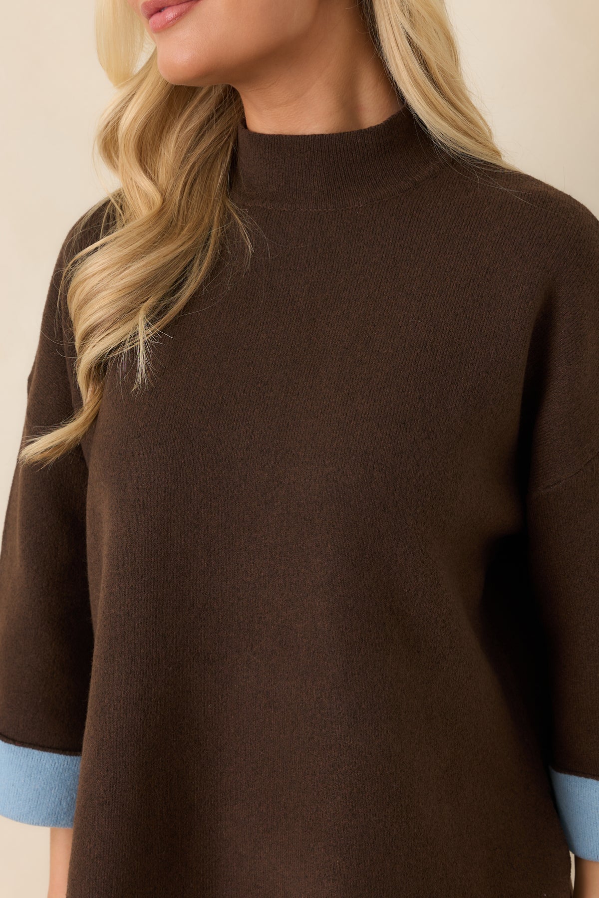 Close-up of the brown knit top highlighting the ribbed mock neckline and light blue turnback cuff contrast.