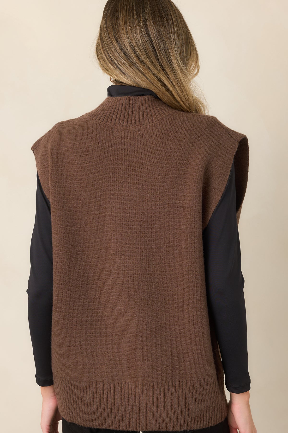 Rear of the warm brown knit vest showing the relaxed silhouette, extended shoulders, and wide ribbed hem.