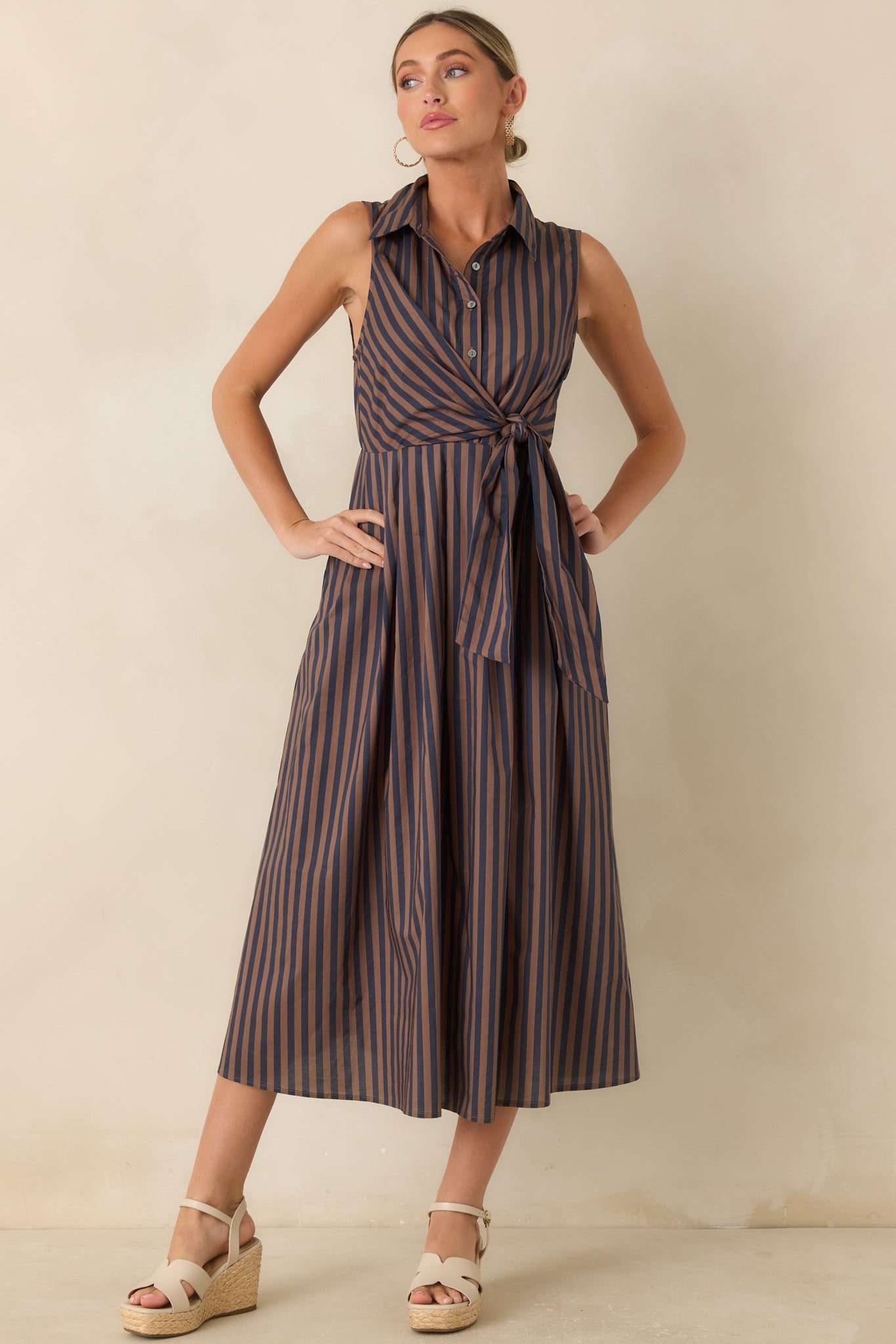 Brown and navy striped midi dress featuring a sleeveless shirtdress design, waist tie detail, pointed collar, and full A-line skirt.