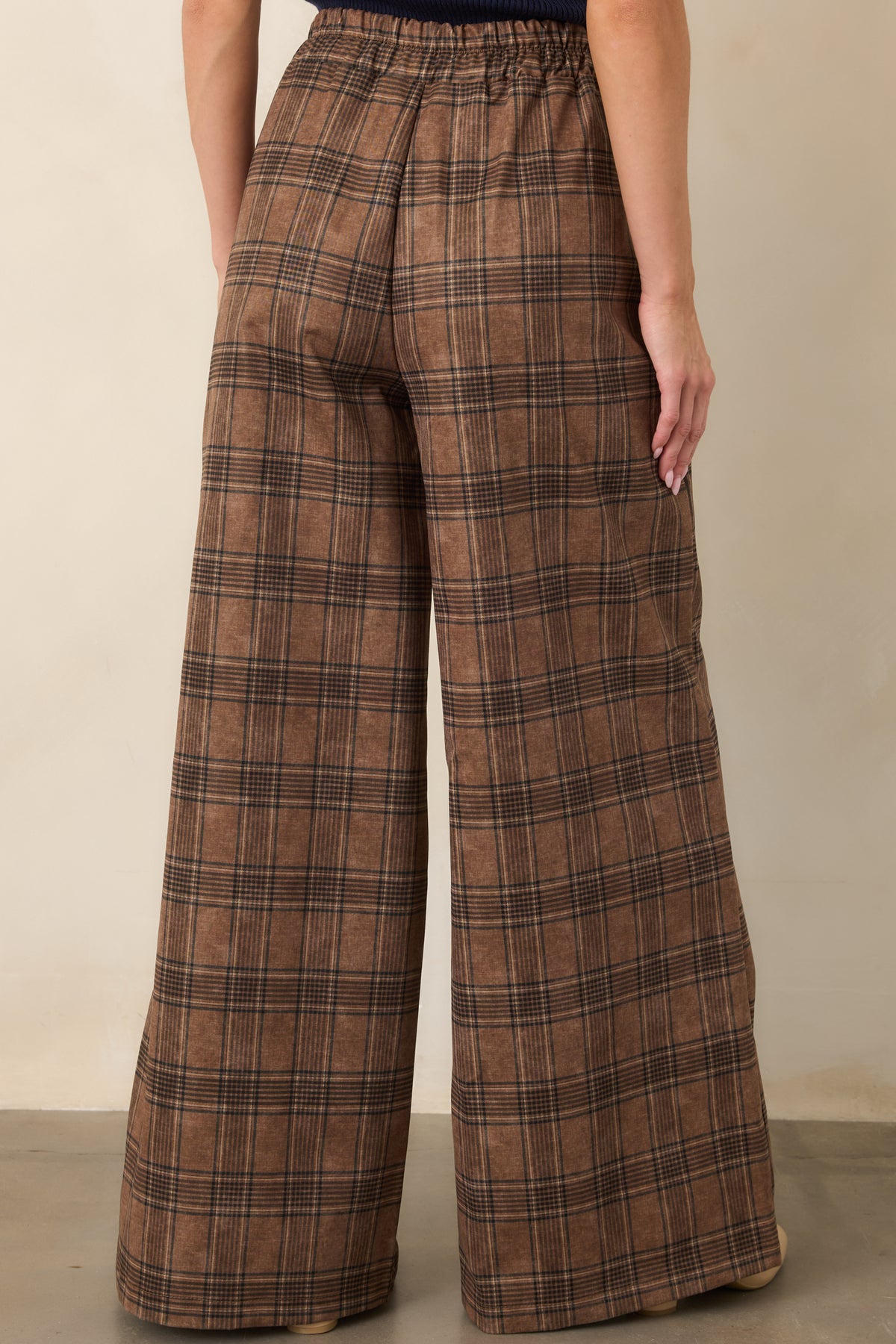 Rear of the brown plaid pants showcasing the high-rise waist and long, sweeping wide-leg silhouette.