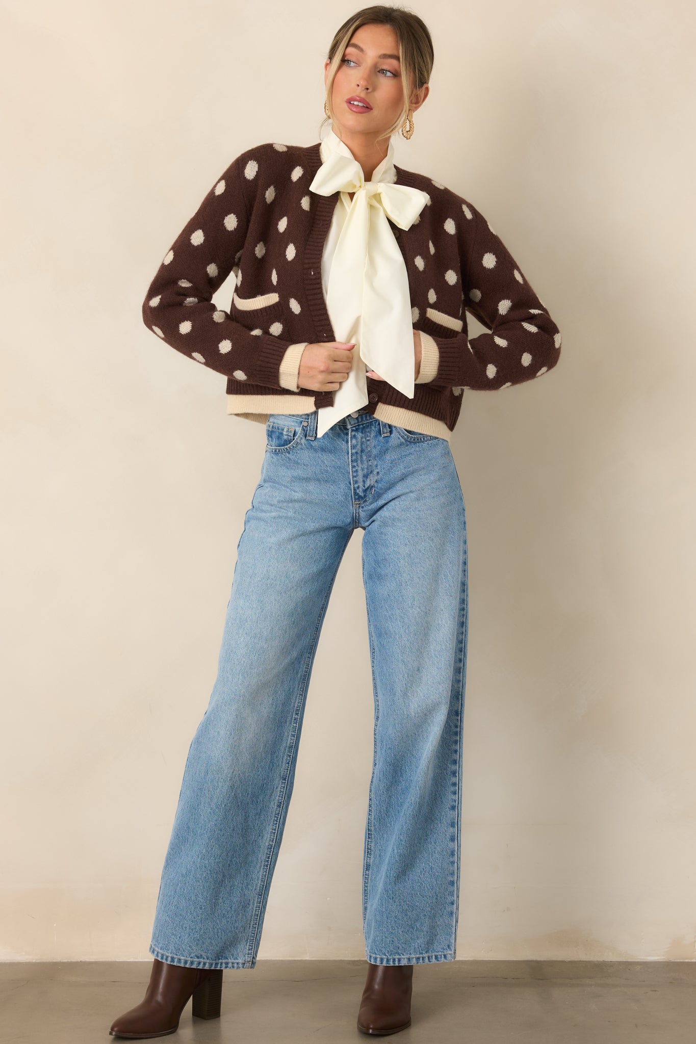 Brown polka dot cardigan with a button closure, ribbed edges, small patch pockets, and layered ivory trim for contrast.