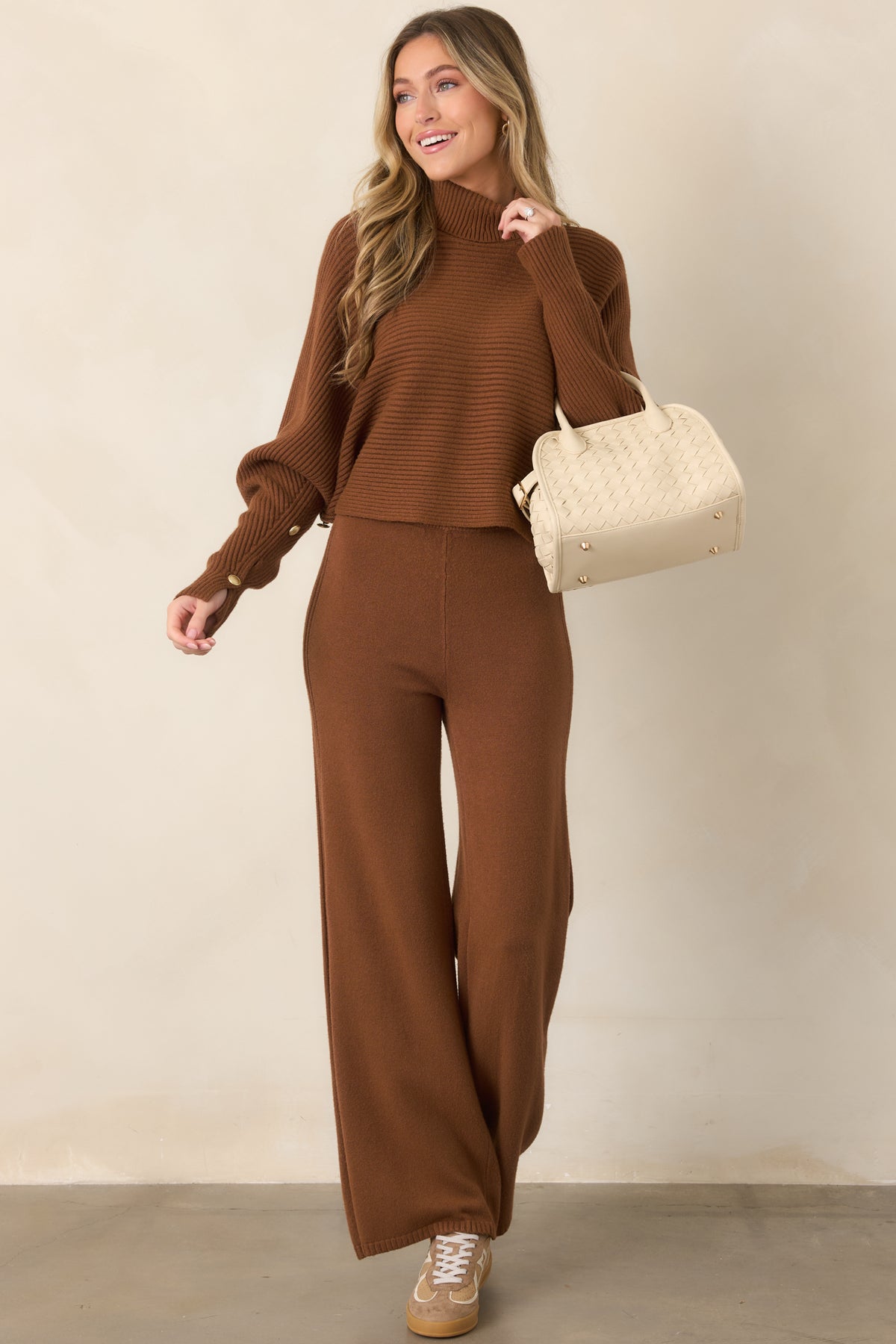Soft brown rib-knit sweater showcasing a relaxed drape, wide batwing sleeves, tall turtleneck collar, and button-detailed cuffs.