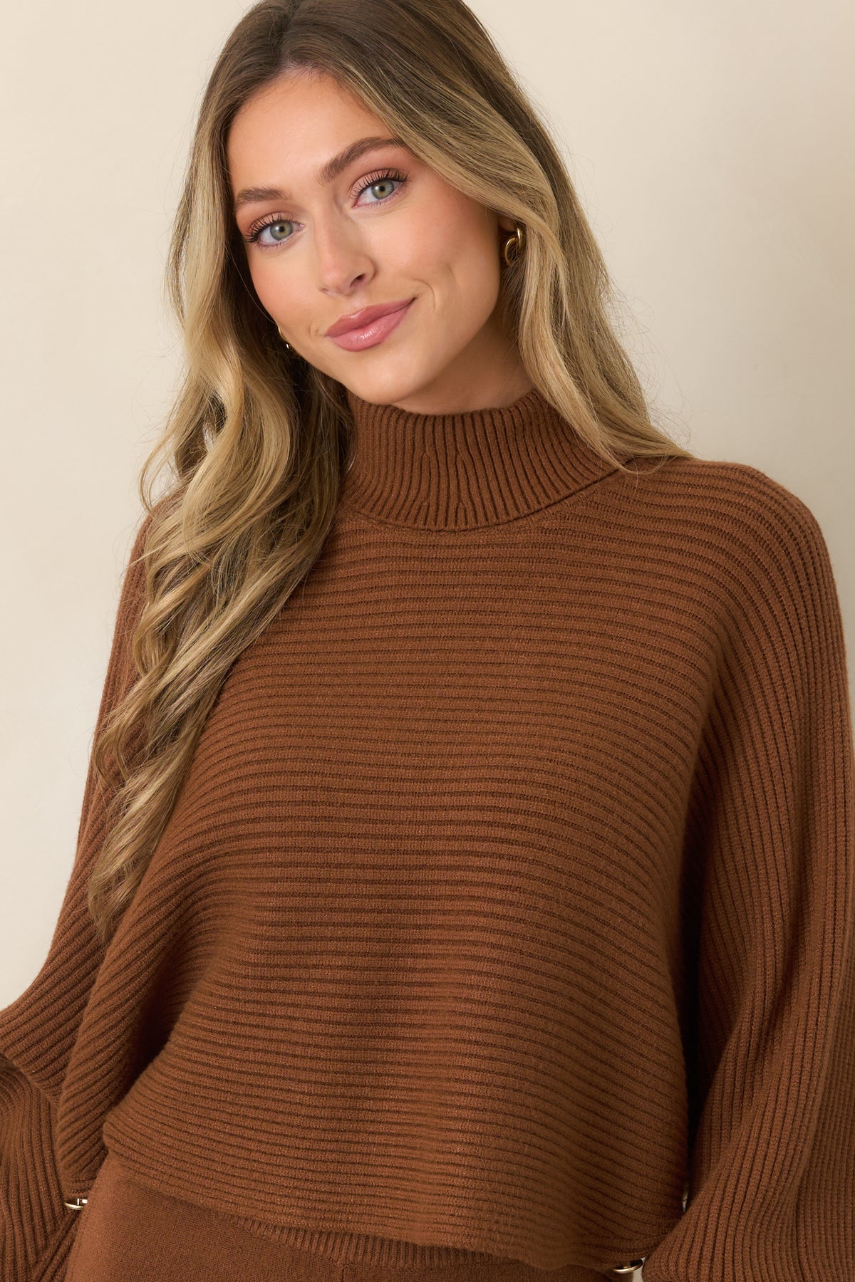 Brown ribbed sweater detail showcasing the fluid sleeve drape, textured knit construction, and cropped lower edge.