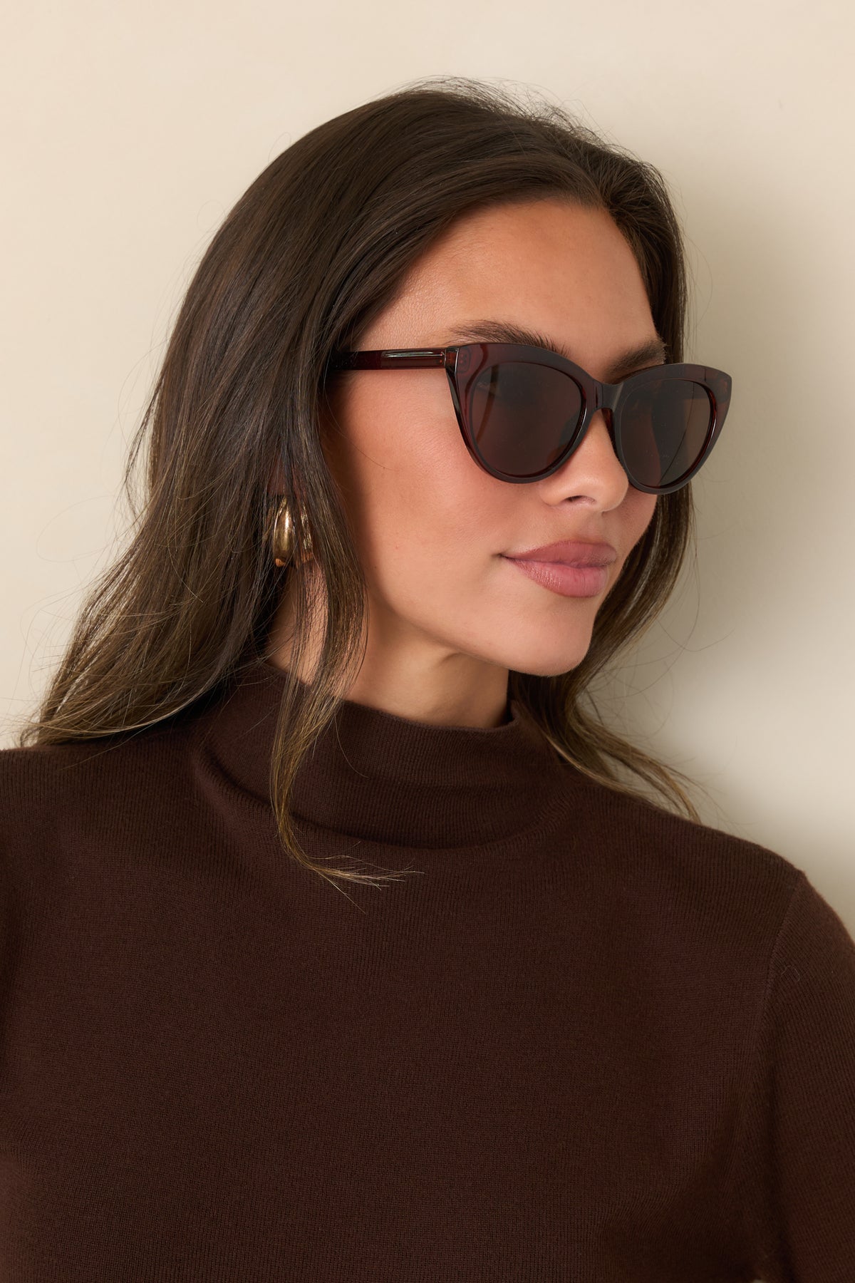 Brown sunglasses feature a rounded cat-eye shape, thin arms, and solid-color lenses for a sleek finish.

