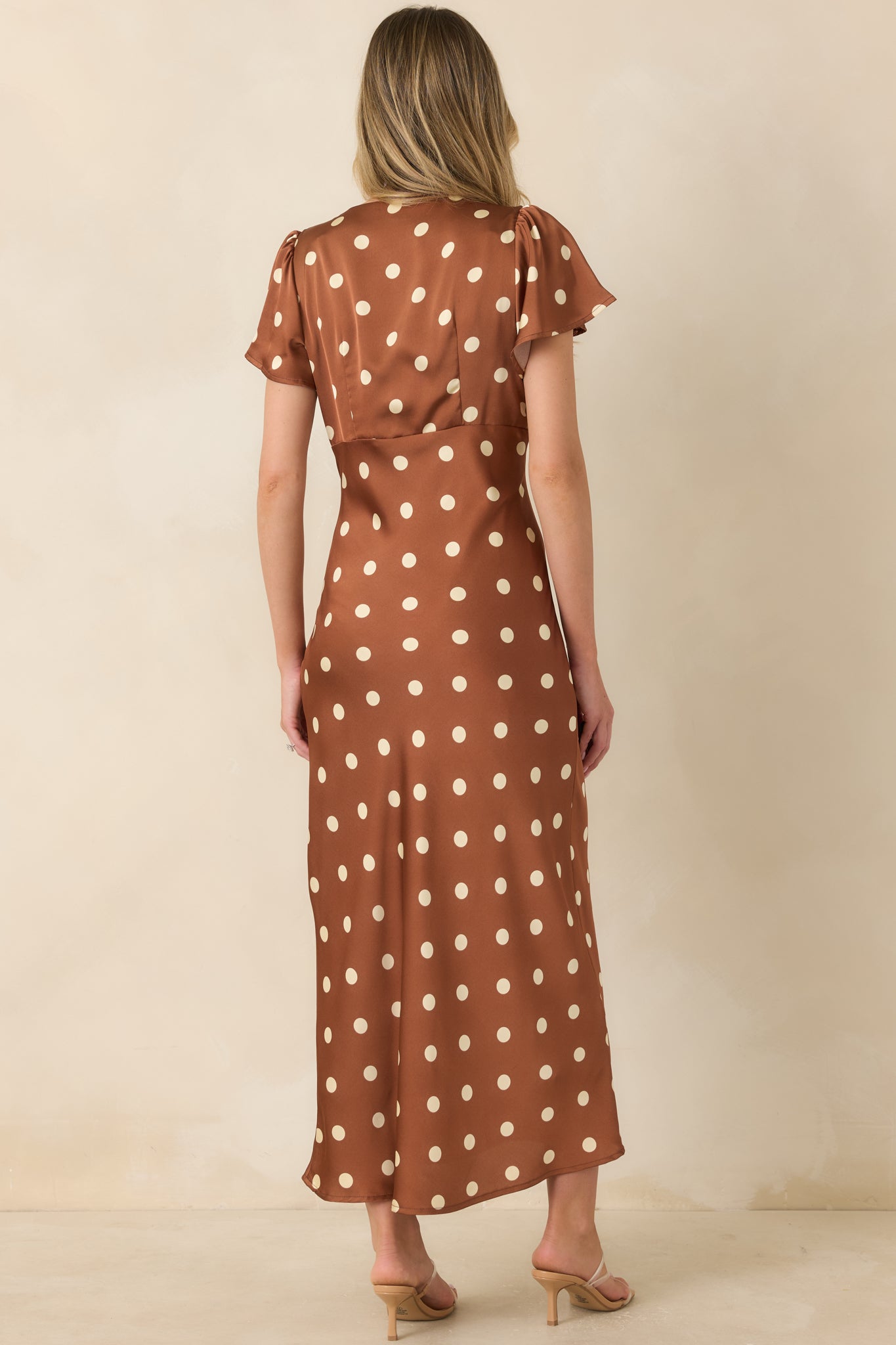 Rear view of the brown satin midi dress featuring a smooth silhouette, flutter sleeves, and flowing skirt.