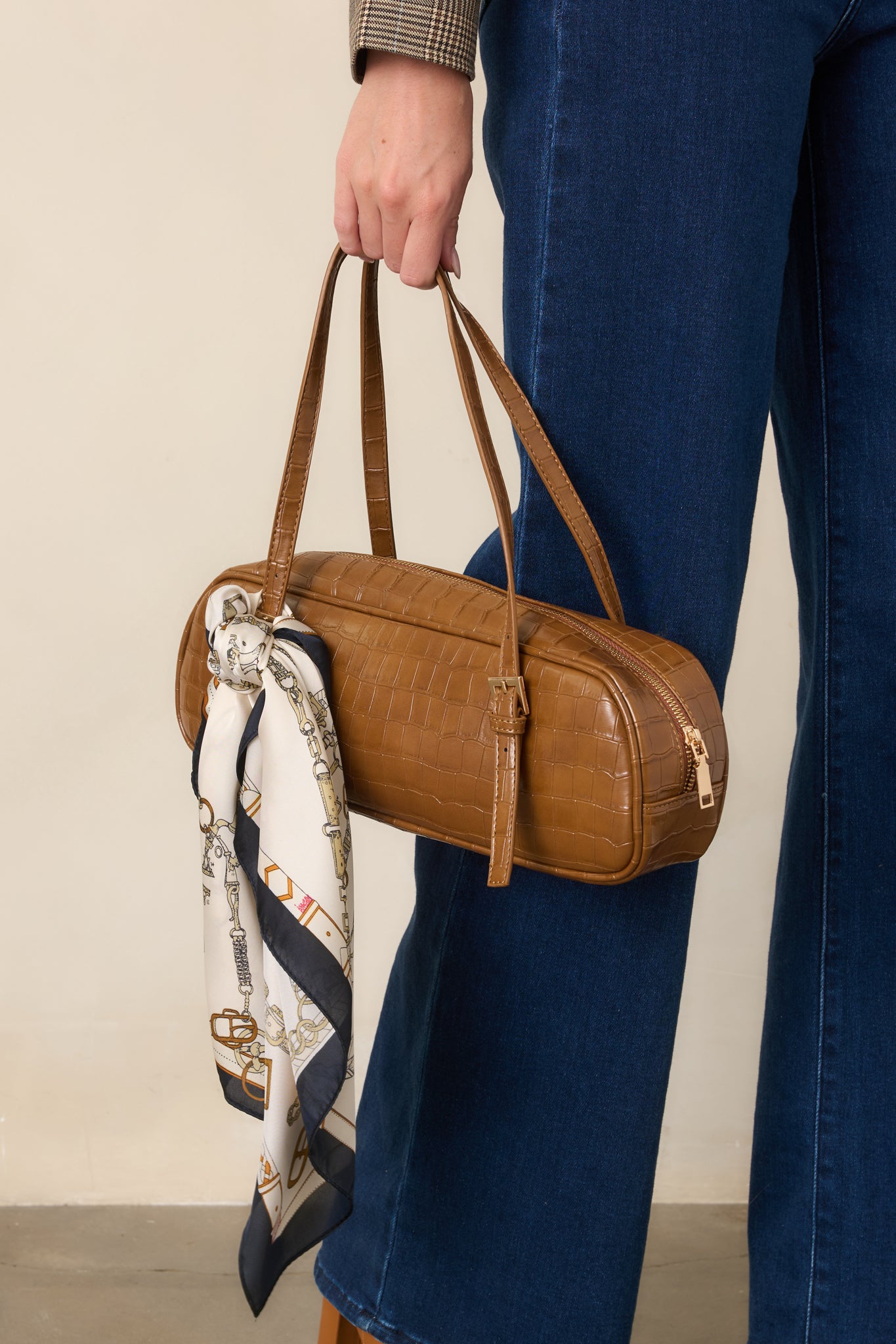 Brown faux leather handbag showcasing the elongated shape, textured exterior, and polished top handle construction.