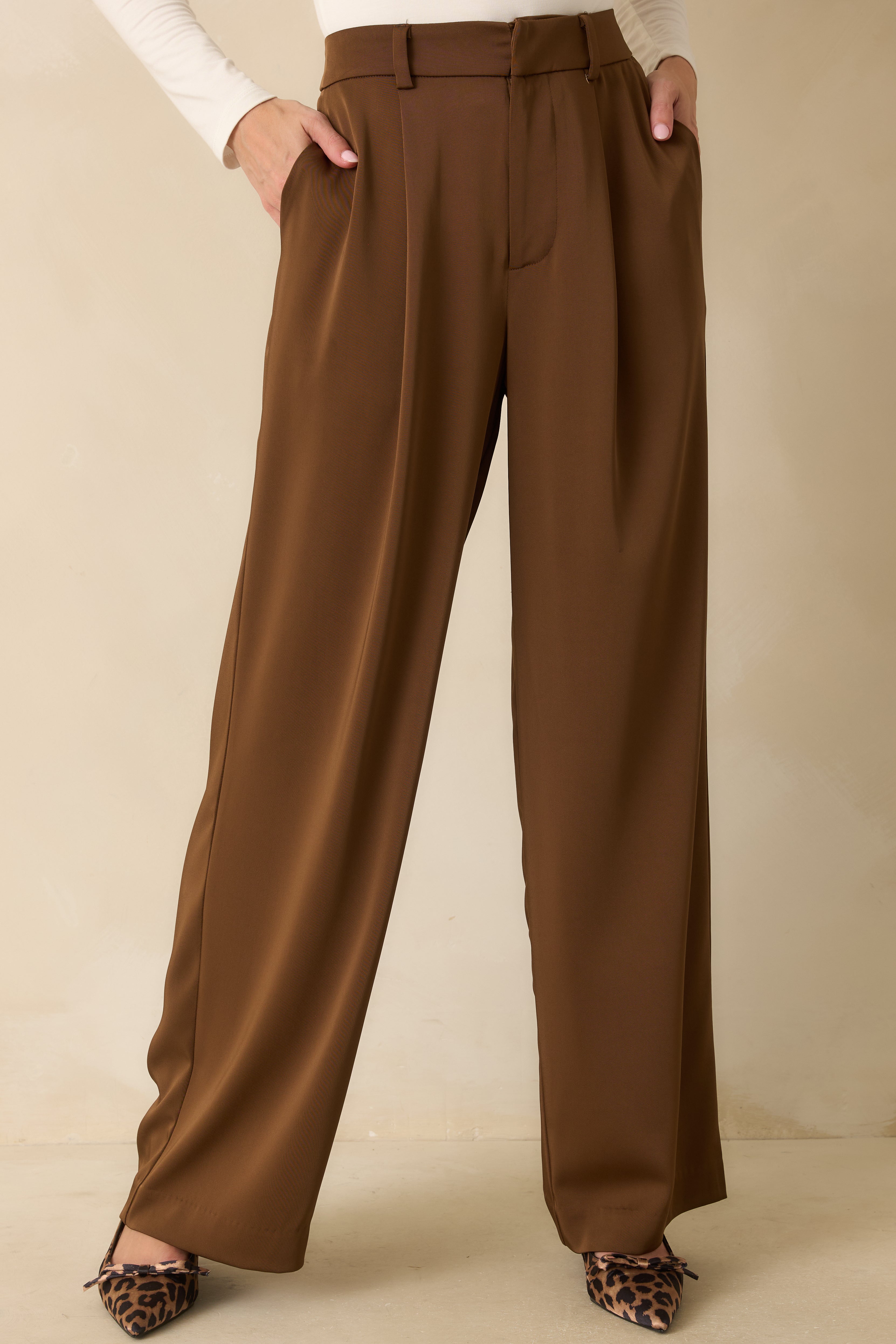 Close-up of the brown trouser fabric and waistband detailing, including pleats and belt loops.