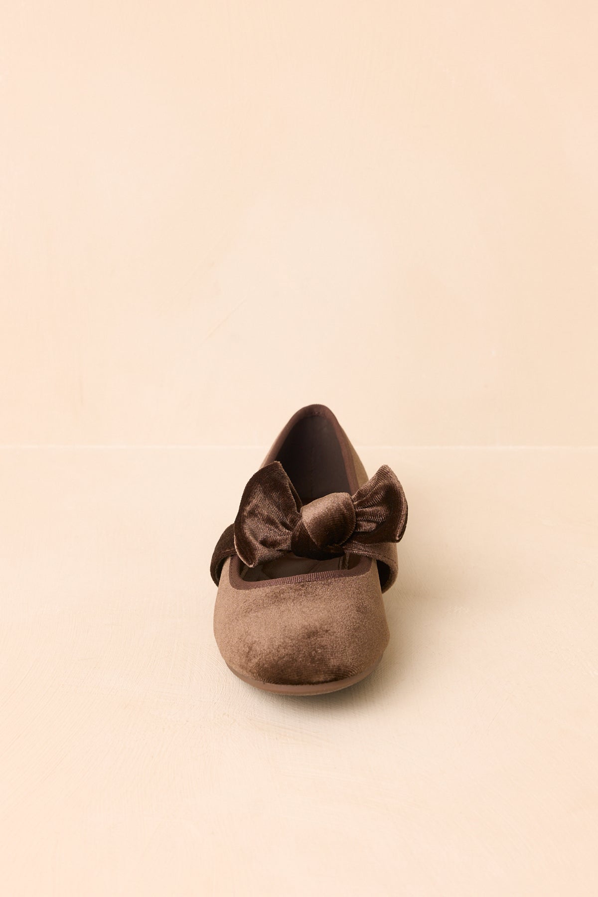 Brown velvet flats highlighting the rounded-toe shape, decorative bow, and petite low heel.
