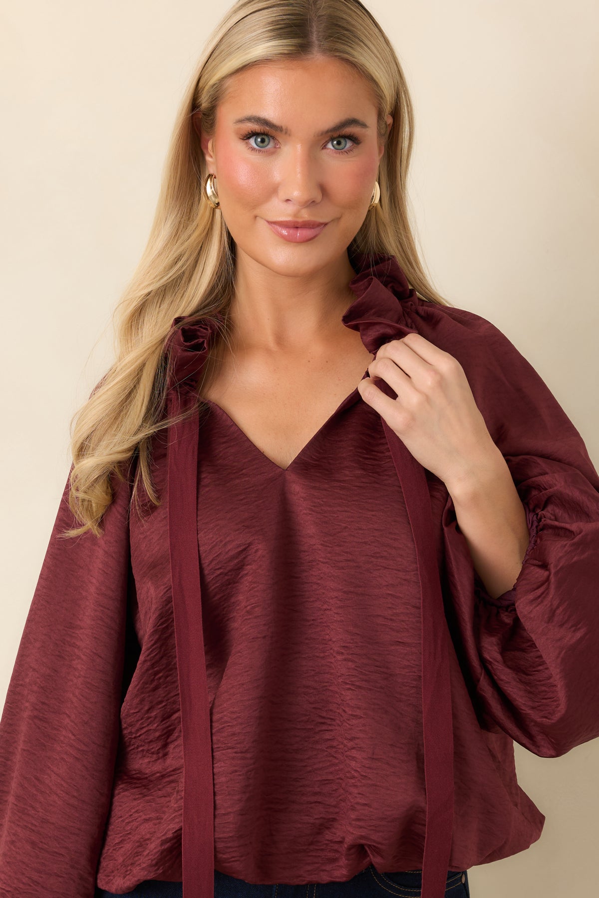 Voluminous balloon sleeves add fullness to the burgundy blouse, highlighting its crinkled texture and subtle sheen.