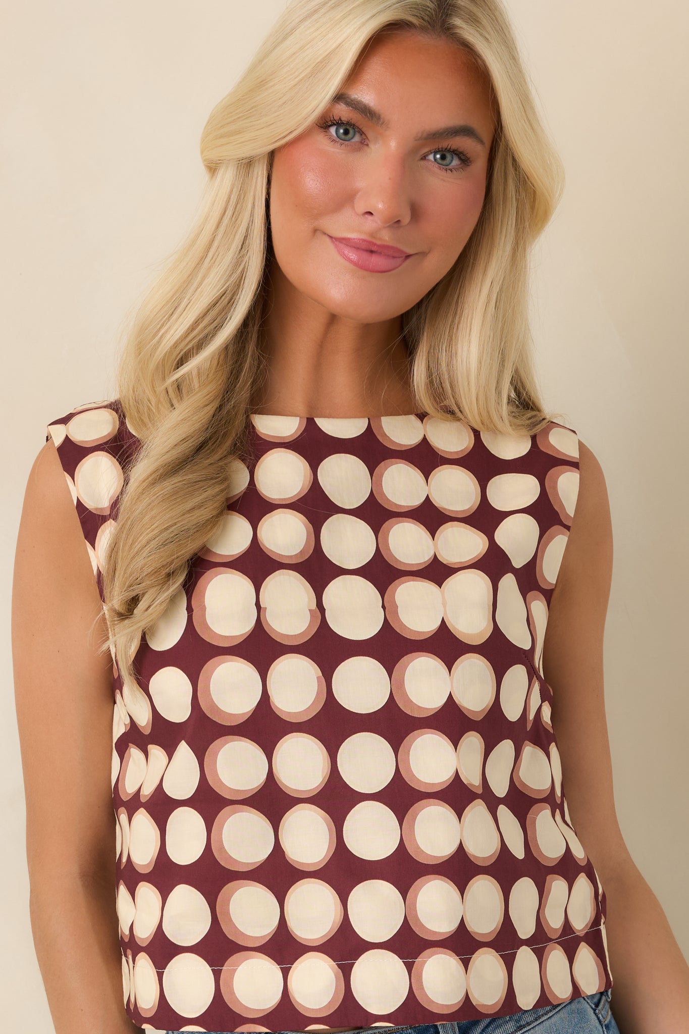 Cropped view of the burgundy top featuring the rounded boat neckline, sleeveless design, and contrasting abstract dot print.