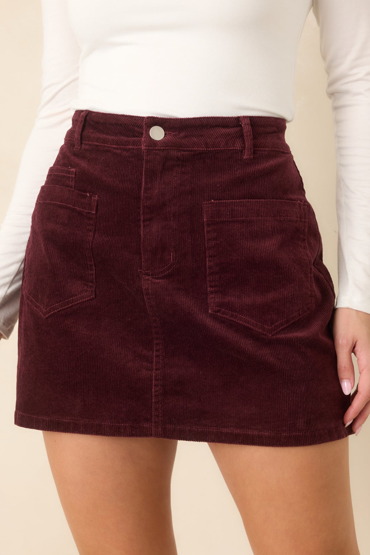 Tonal stitching outlines the front pockets and gently flared shape of the burgundy corduroy skirt.