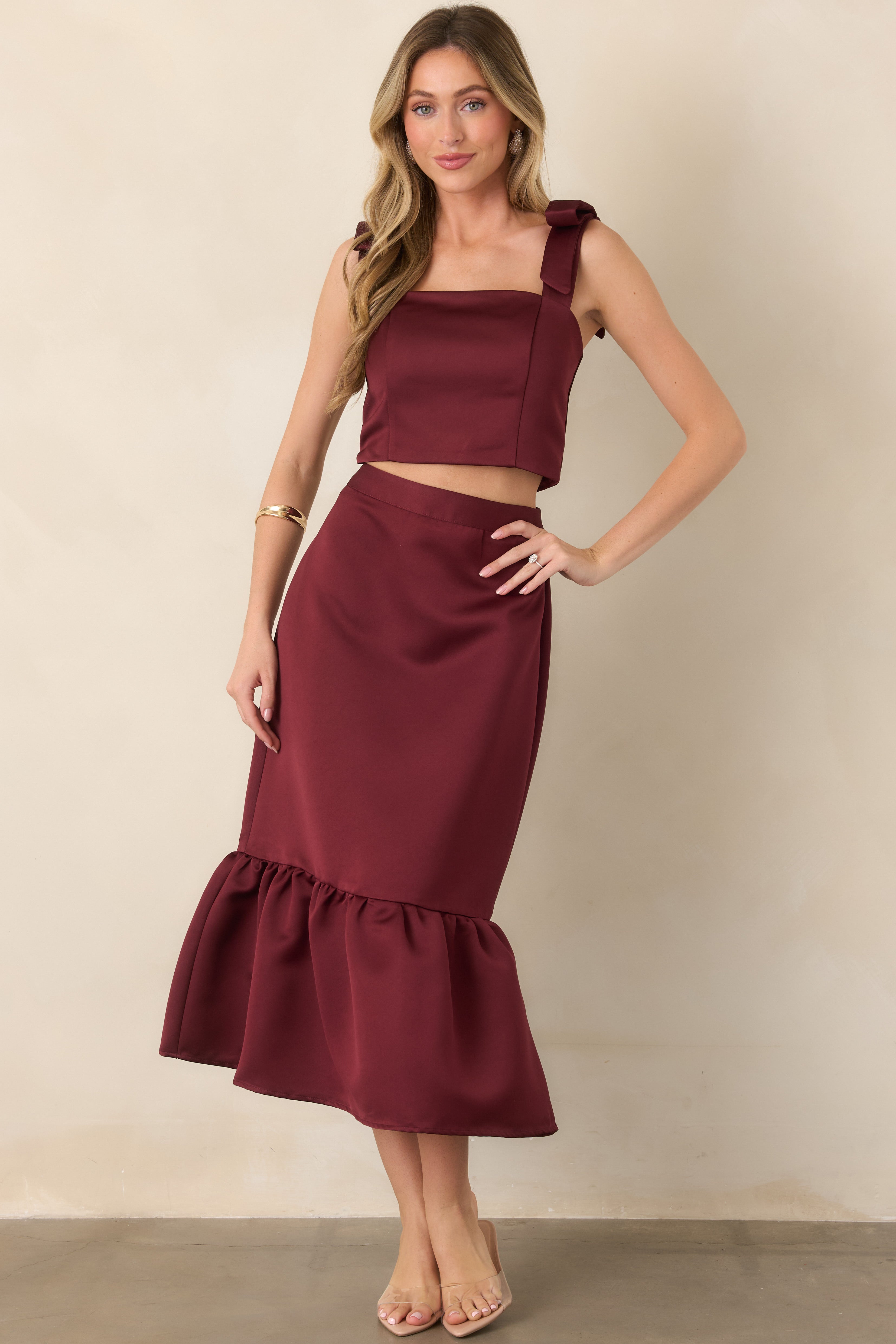 Rich burgundy satin top showcasing its cropped silhouette, elegant square neckline, and delicate bow accents at the shoulders.