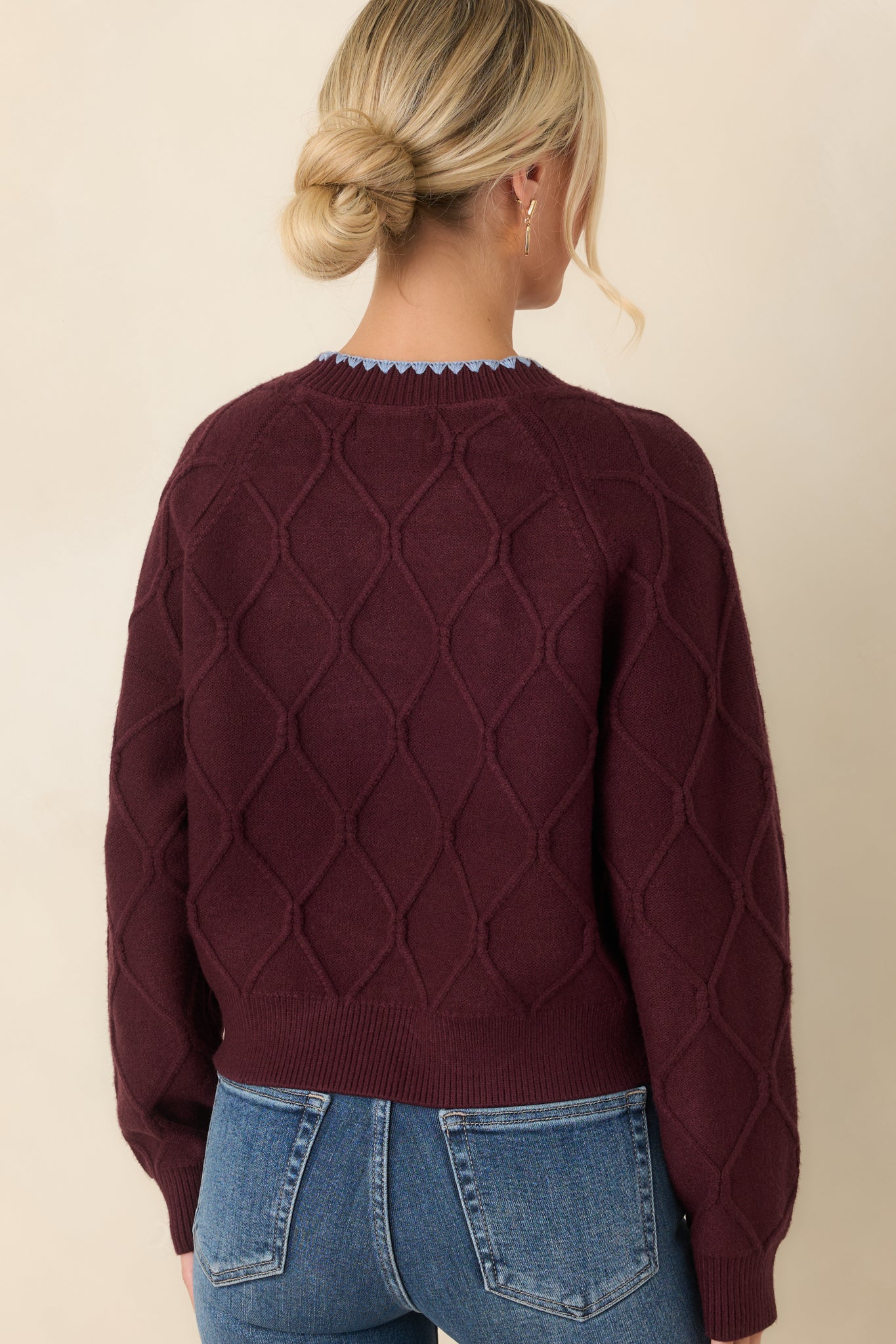 Rear view of the burgundy diamond-knit sweater featuring a textured back, long sleeves, ribbed cuffs, and a relaxed cropped silhouette.