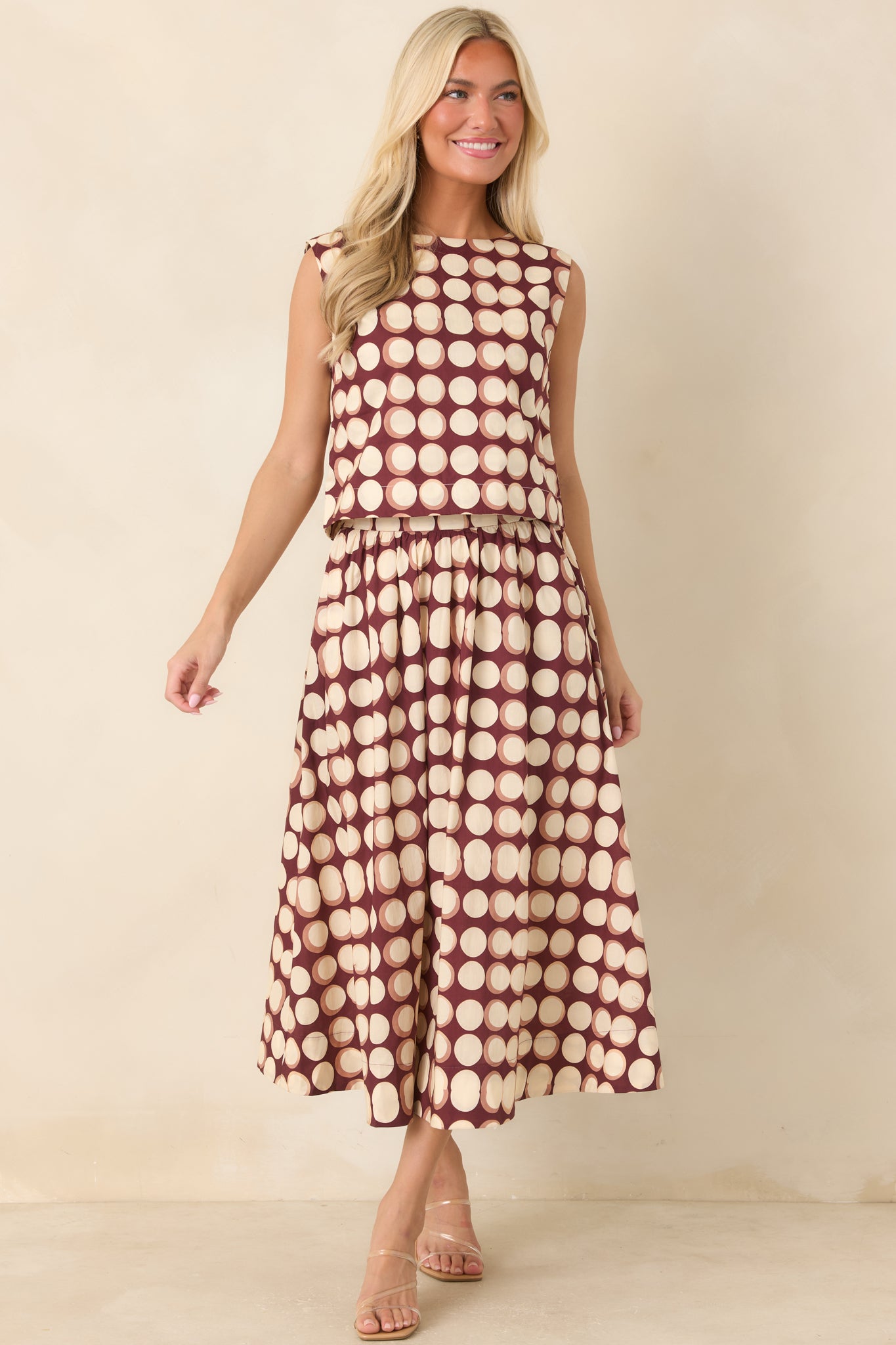 Sleeveless cropped top showcasing an ivory and muted tan abstract dot pattern against a rich burgundy background and clean boat neckline.