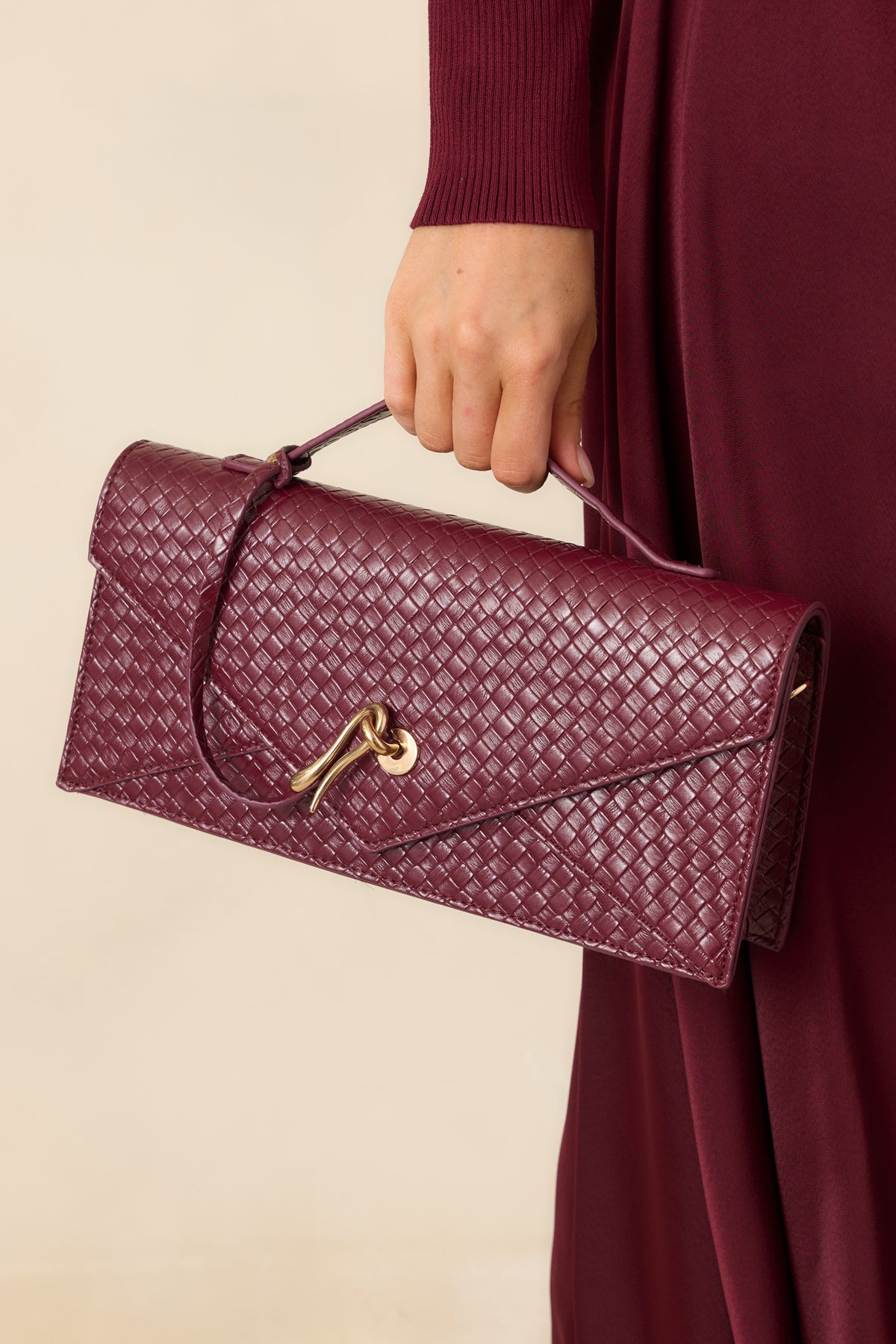 Structured burgundy envelope clutch featuring a slender top handle and detachable gold-tone chain strap.