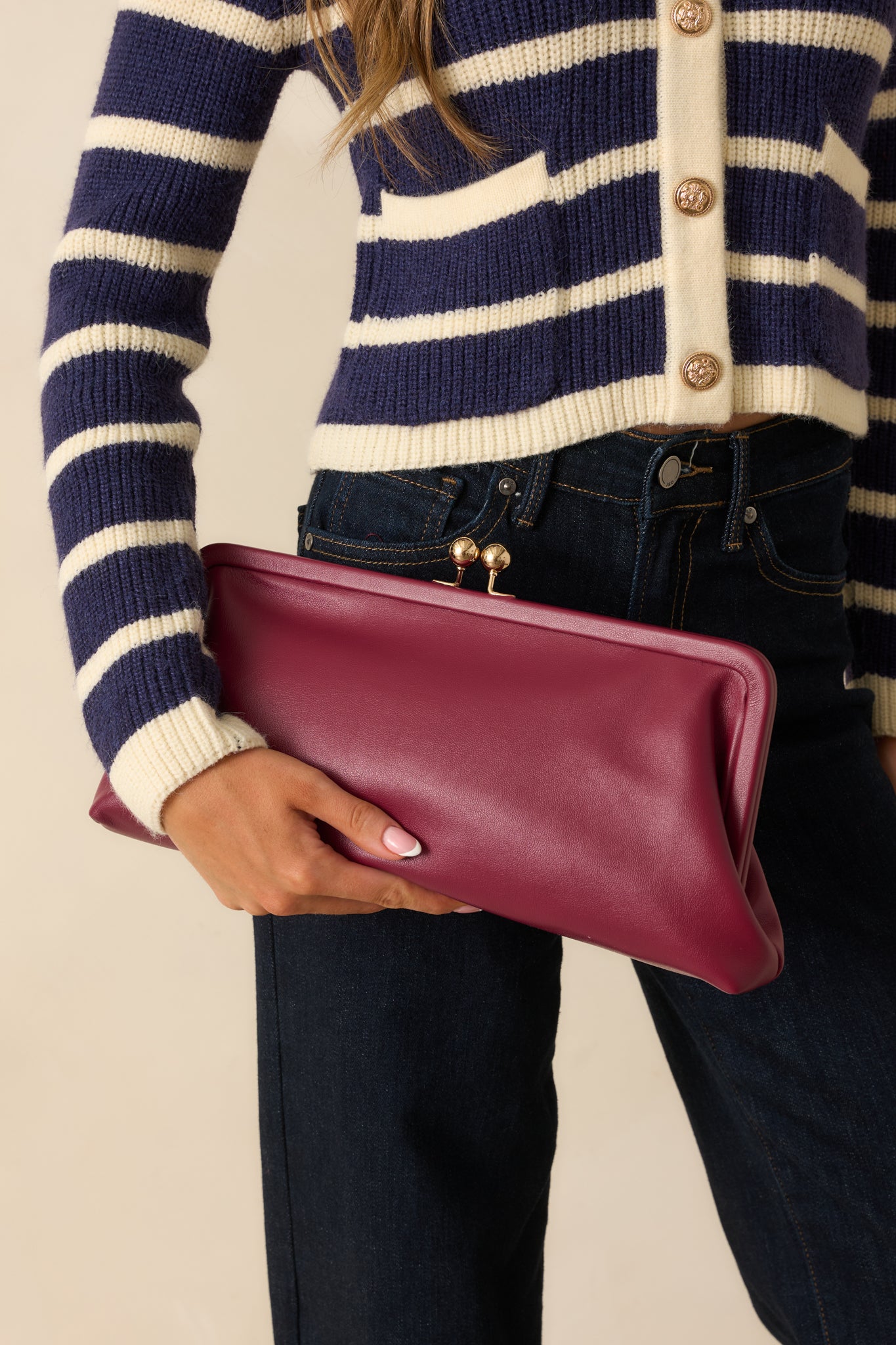 Front view of burgundy clutch handbag featuring smooth faux leather exterior and elegant gold clasp.