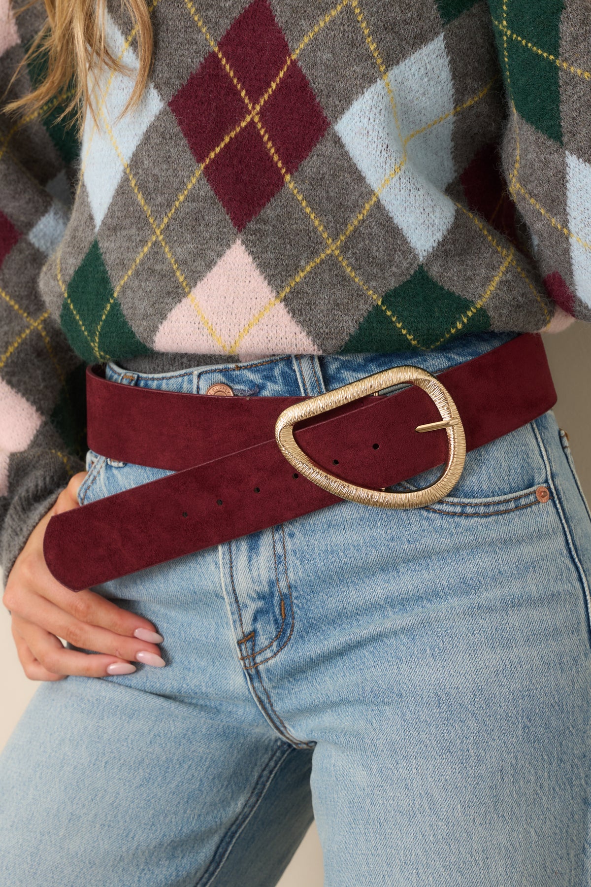 Wide burgundy faux suede belt with an oversized asymmetrical gold-tone buckle and multiple adjustment holes.