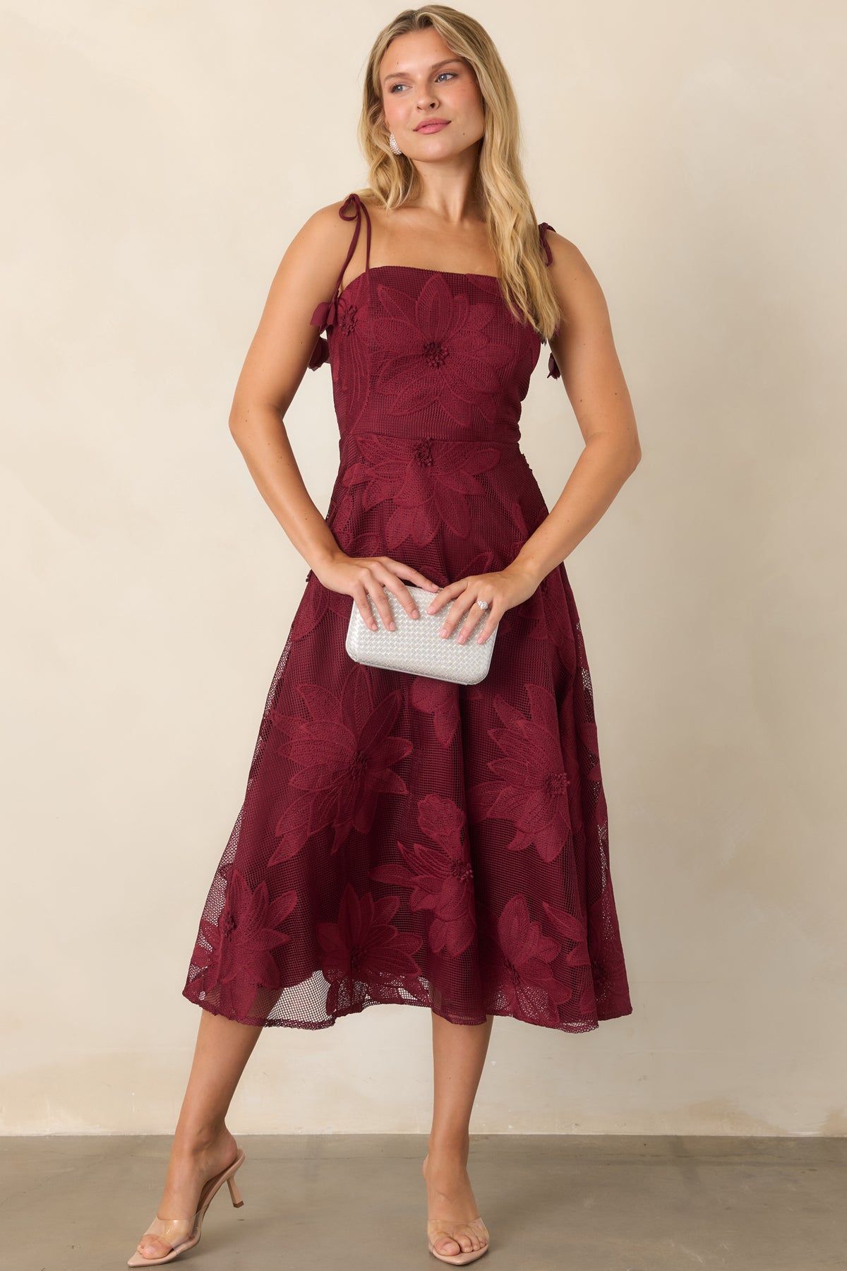 Burgundy floral lace dress featuring a defined bodice, romantic tie straps, and flowing skirt.