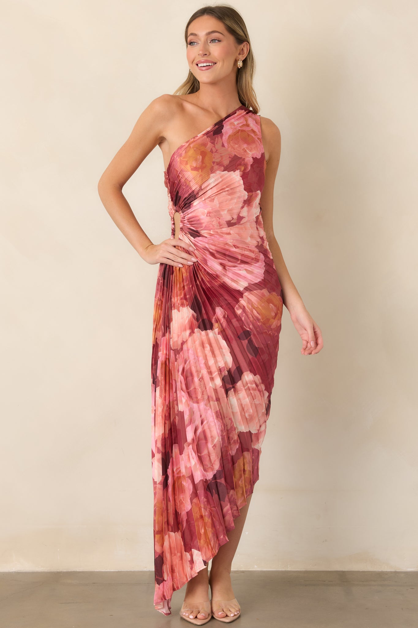 Statement floral maxi dress featuring richly shaded pink and burgundy blooms, a one-shoulder top, fitted waist, dimensional pleats, and an elongated asymmetrical hem.