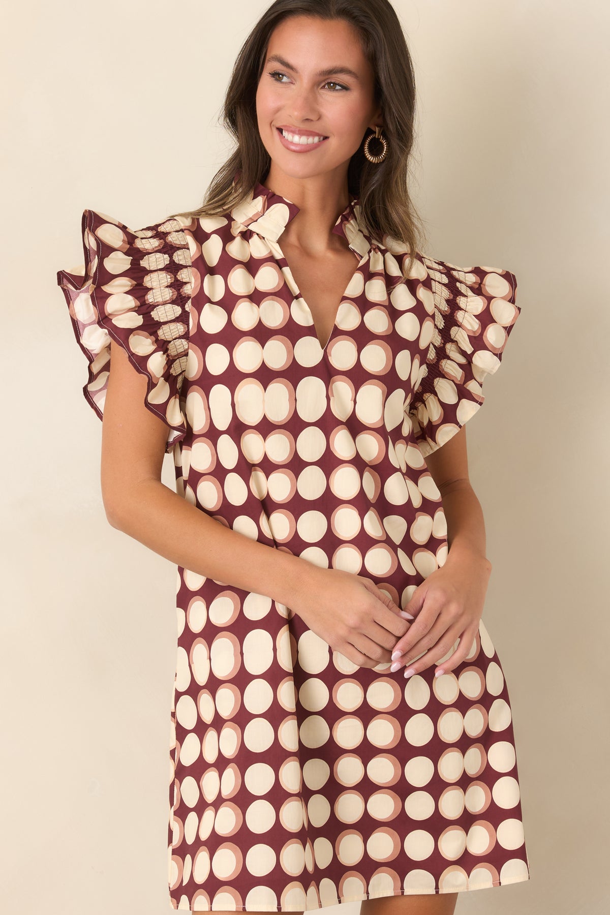 Close view of the relaxed burgundy mini dress featuring graphic ivory dots, short flutter sleeves, and romantic ruffle detailing.