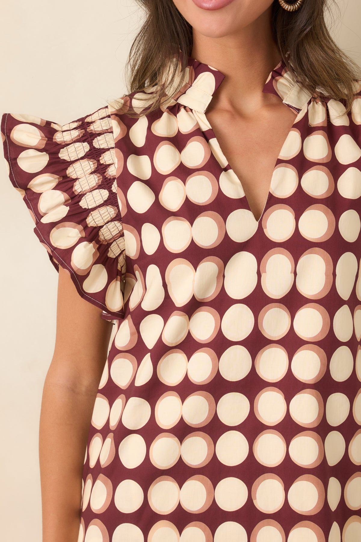 Close-up of the burgundy cotton dress showing the oversized ivory dot print, ruffled stand collar, split neckline, and gathered sleeve detailing.