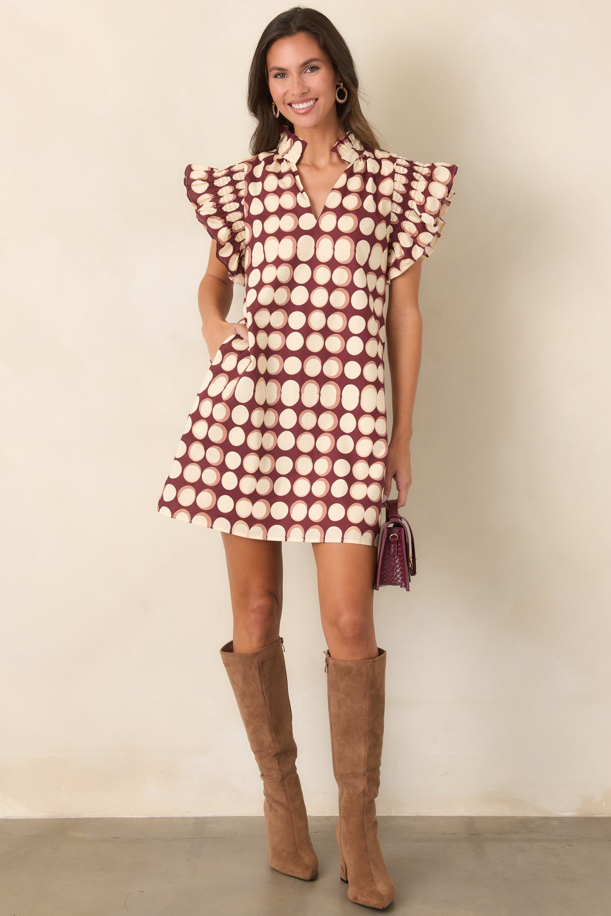 Relaxed burgundy shift mini dress featuring a bold ivory dot pattern, flutter sleeves, ruffled edges, and split neckline.