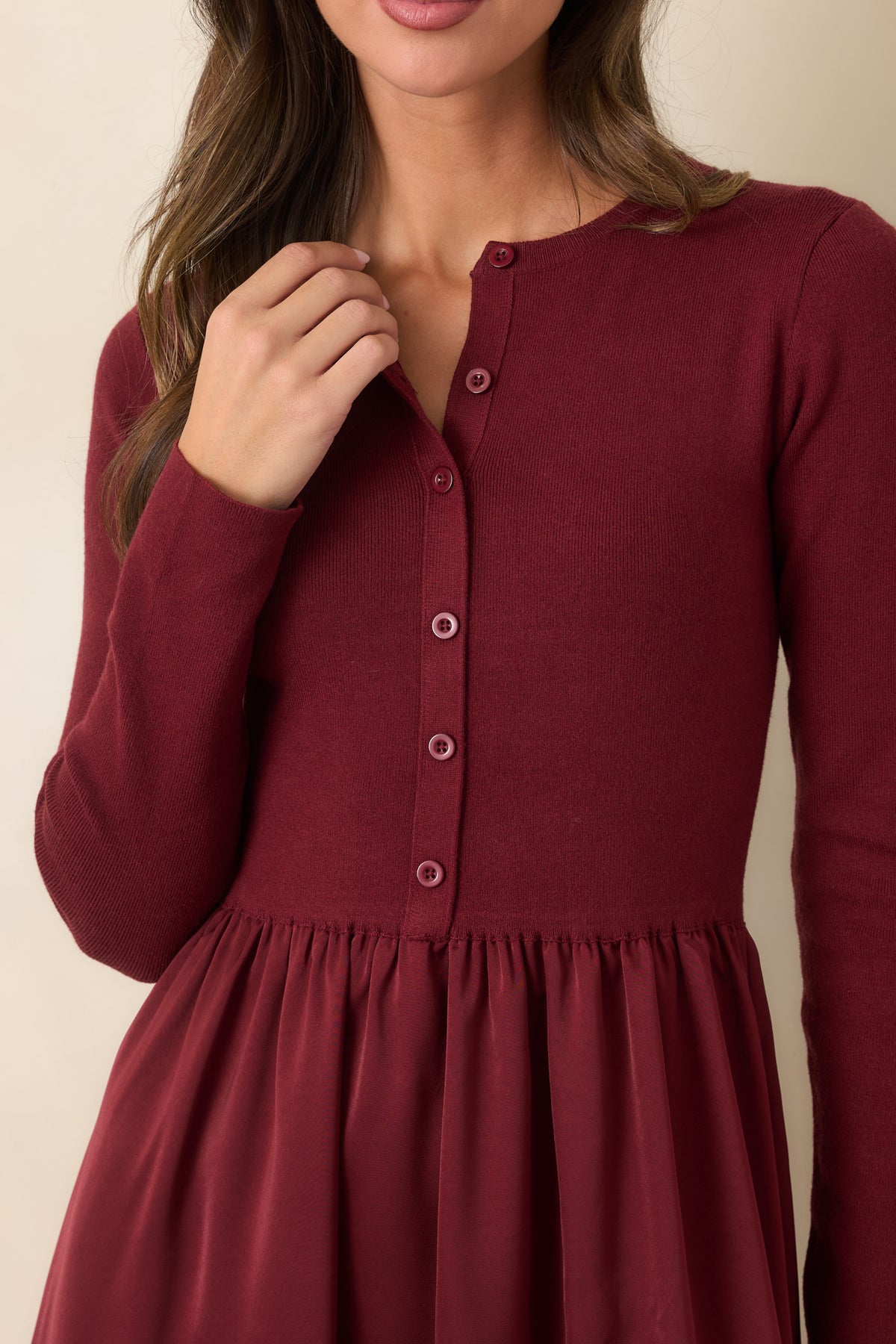 Close-up of the burgundy knit bodice, round neckline, tonal buttons, and gathered satin skirt transition.

