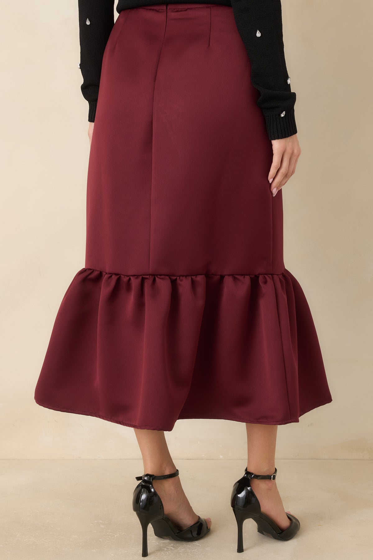 Rear of the burgundy satin midi skirt showing its fitted silhouette and gathered flounce hem.