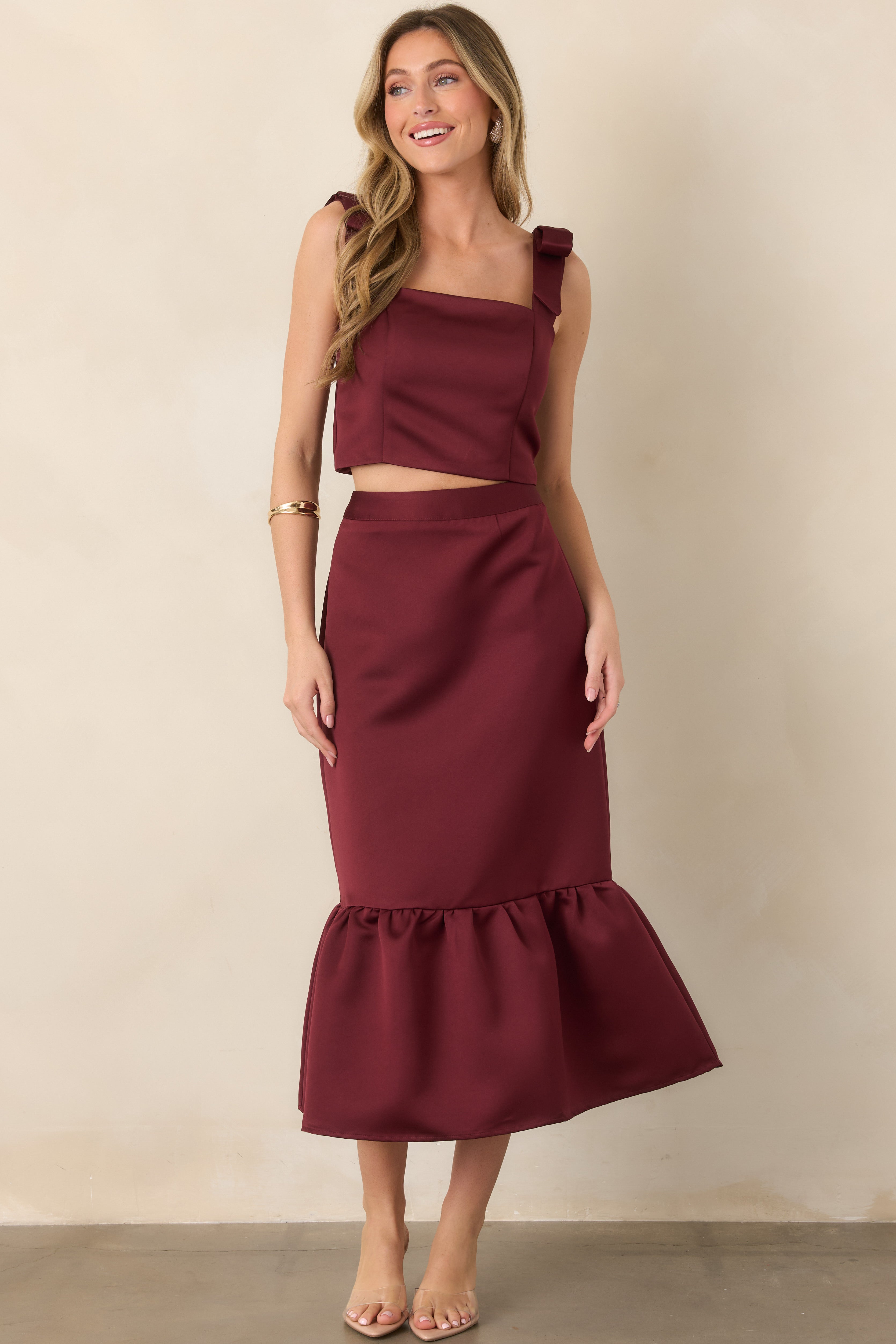 Burgundy satin midi skirt featuring a smooth lustrous finish, fitted silhouette, and gathered flounce hem for added movement and volume.