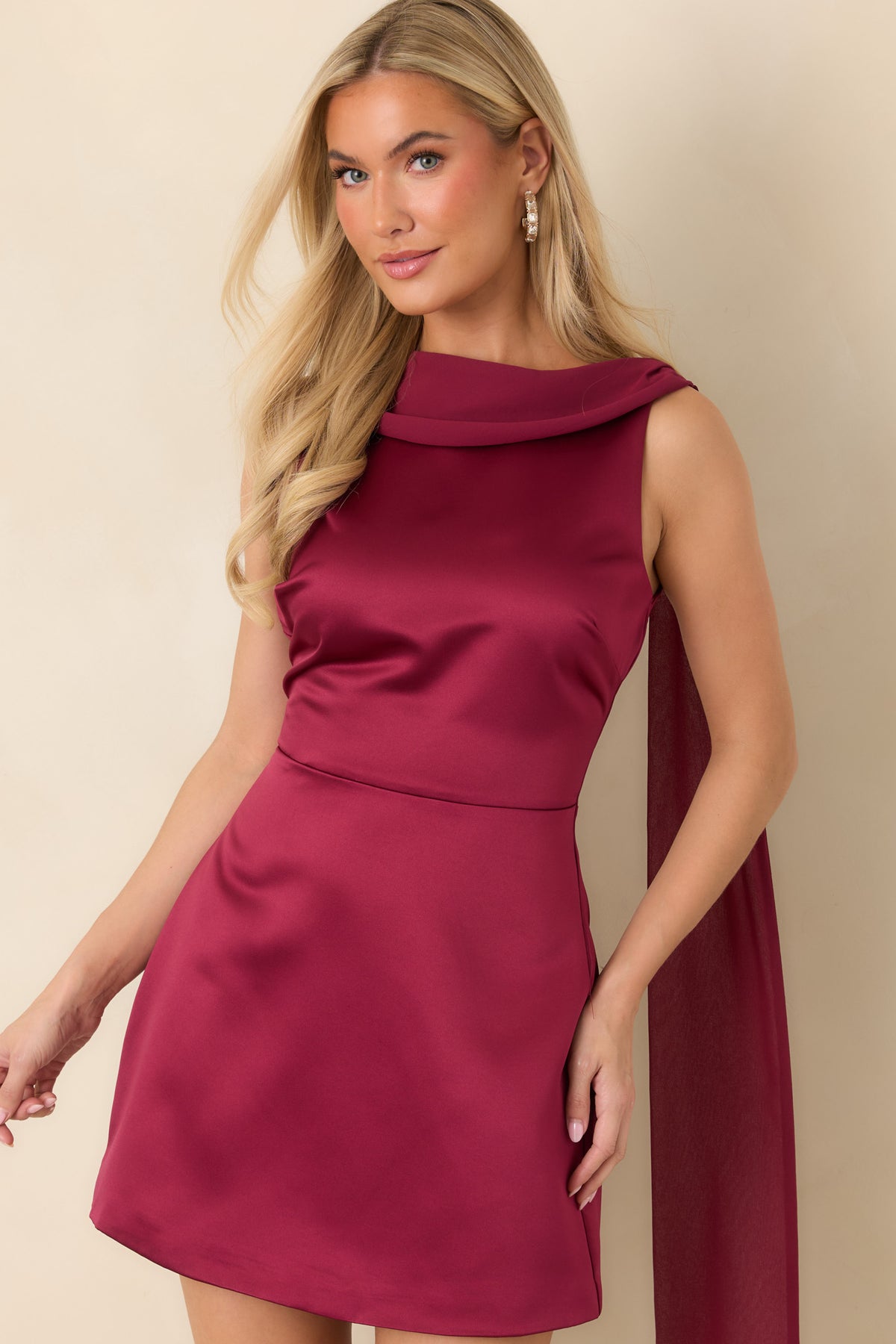 Close view of burgundy satin mini dress highlighting its smooth sheen, high neckline, and draped scarf collar.