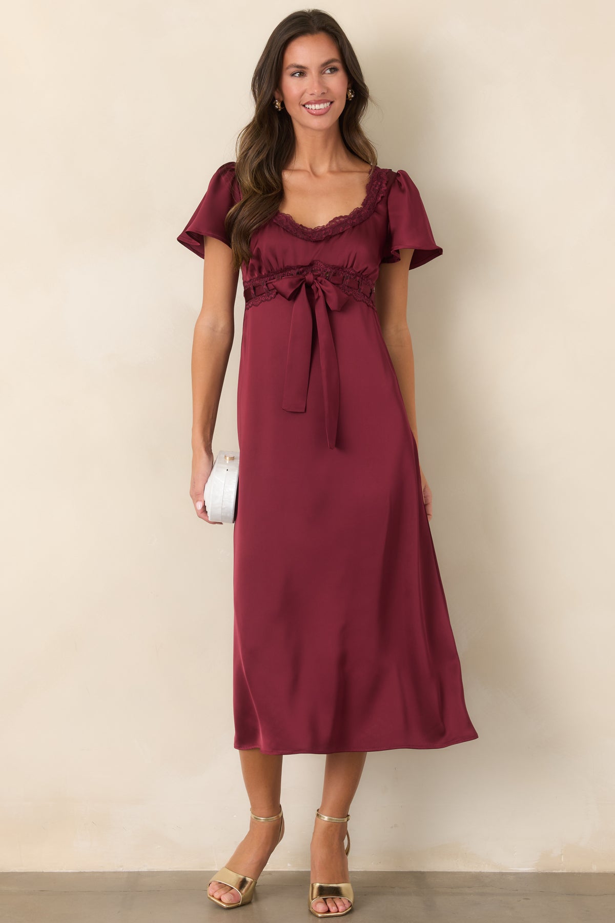 Burgundy satin dress with a scoop neckline, delicate lace trim, and a ribbon bow at the front waist.