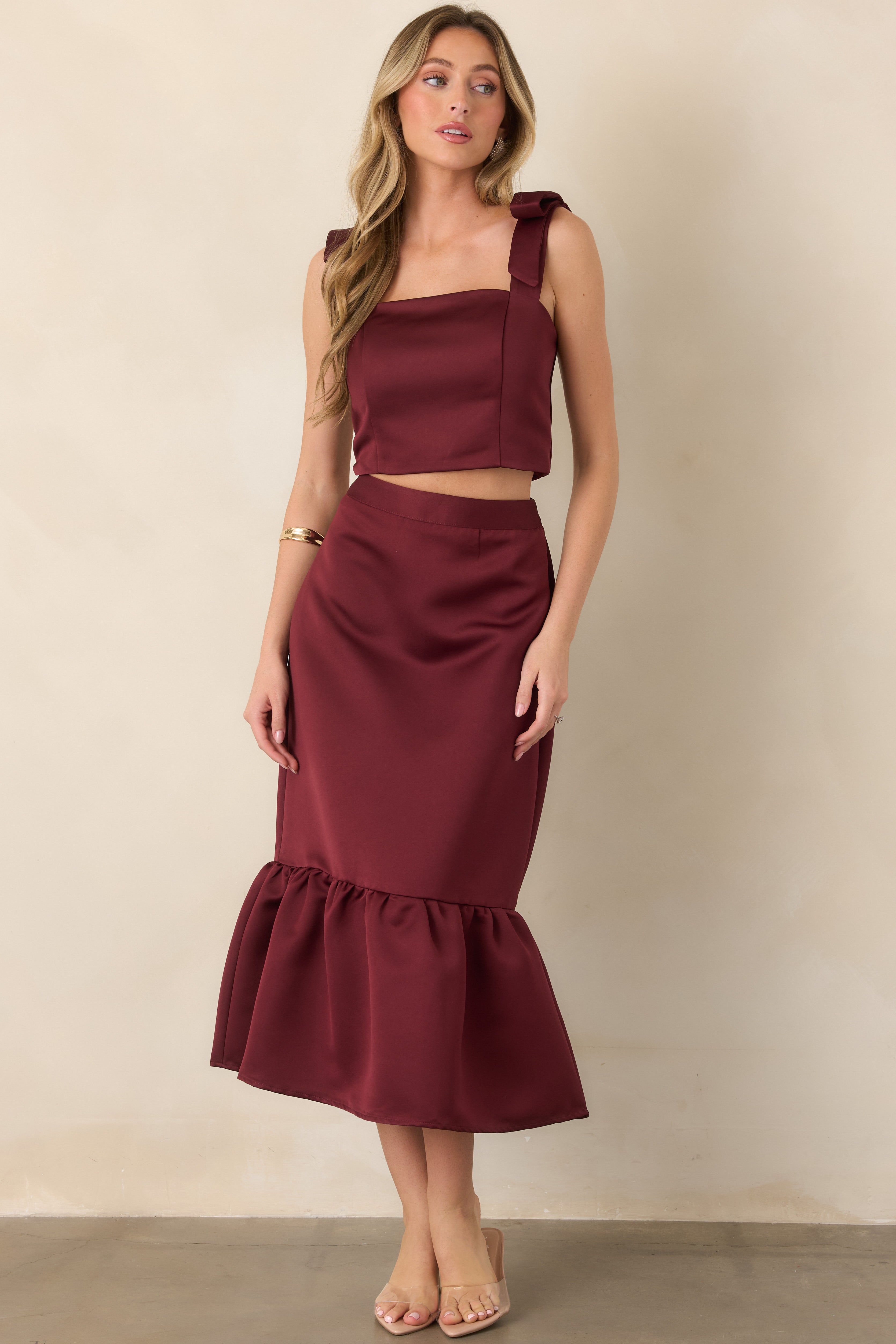 Burgundy satin cropped top featuring a structured square neckline, feminine shoulder bows, and a defined silhouette with a smooth lustrous finish.