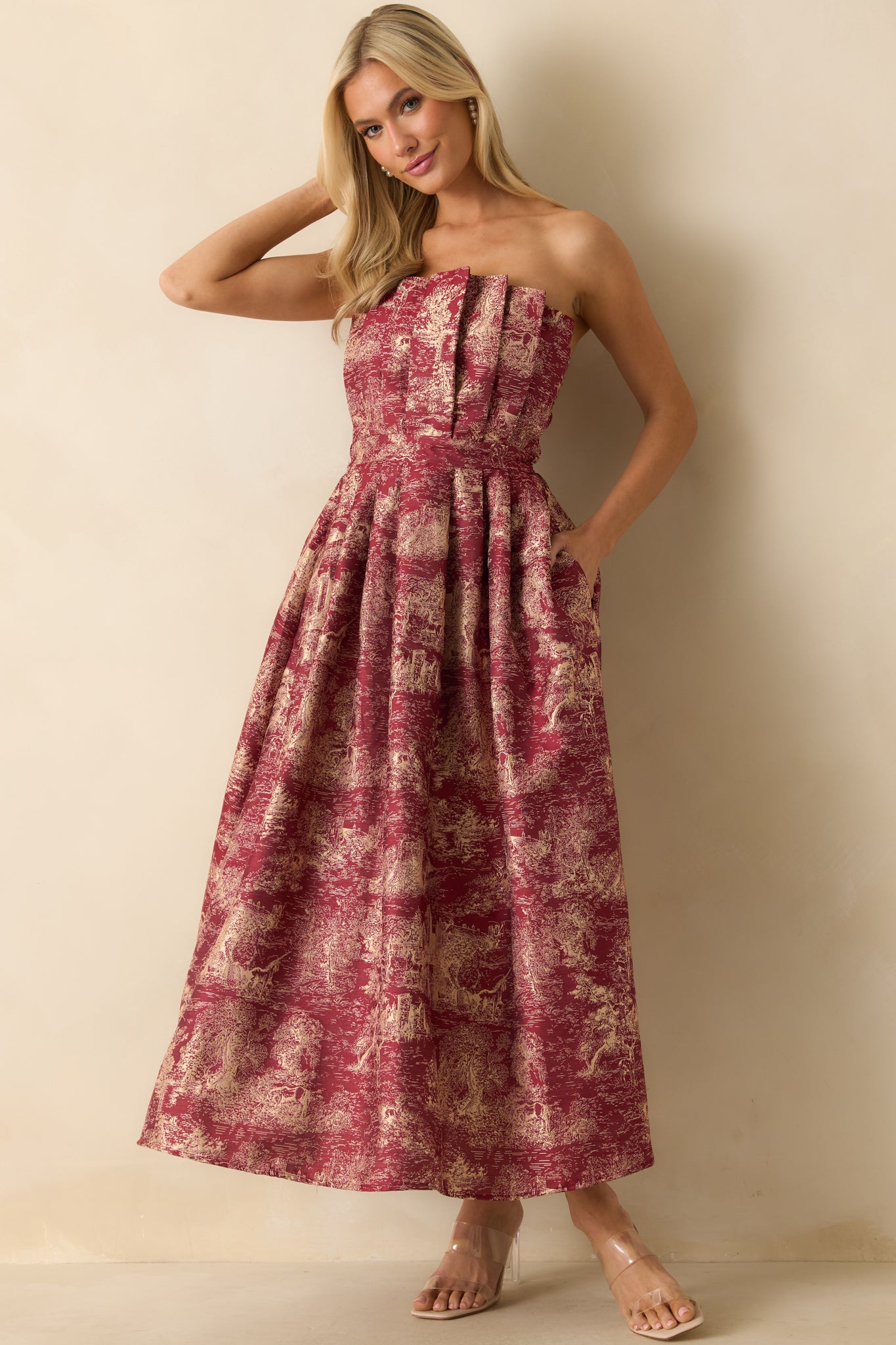 Burgundy strapless midi dress with an ivory jacquard pattern featuring castle and unicorn motifs, pleated structured bodice, and voluminous A-line skirt.