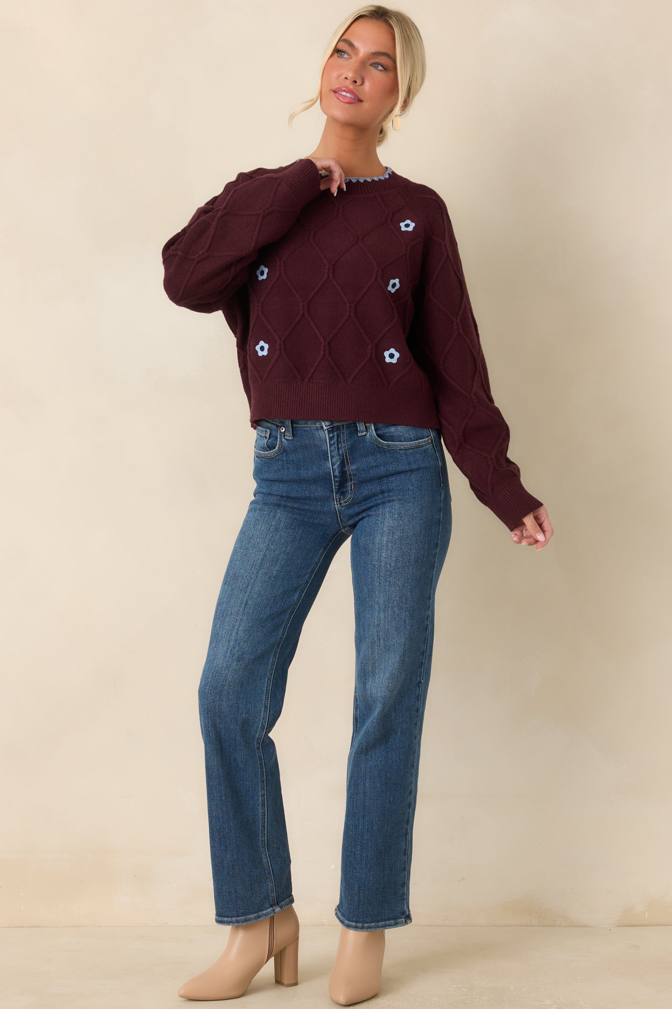 Burgundy knit sweater featuring a raised textured pattern, decorative blue floral accents along the front, scalloped neckline, and cozy ribbed finishes.