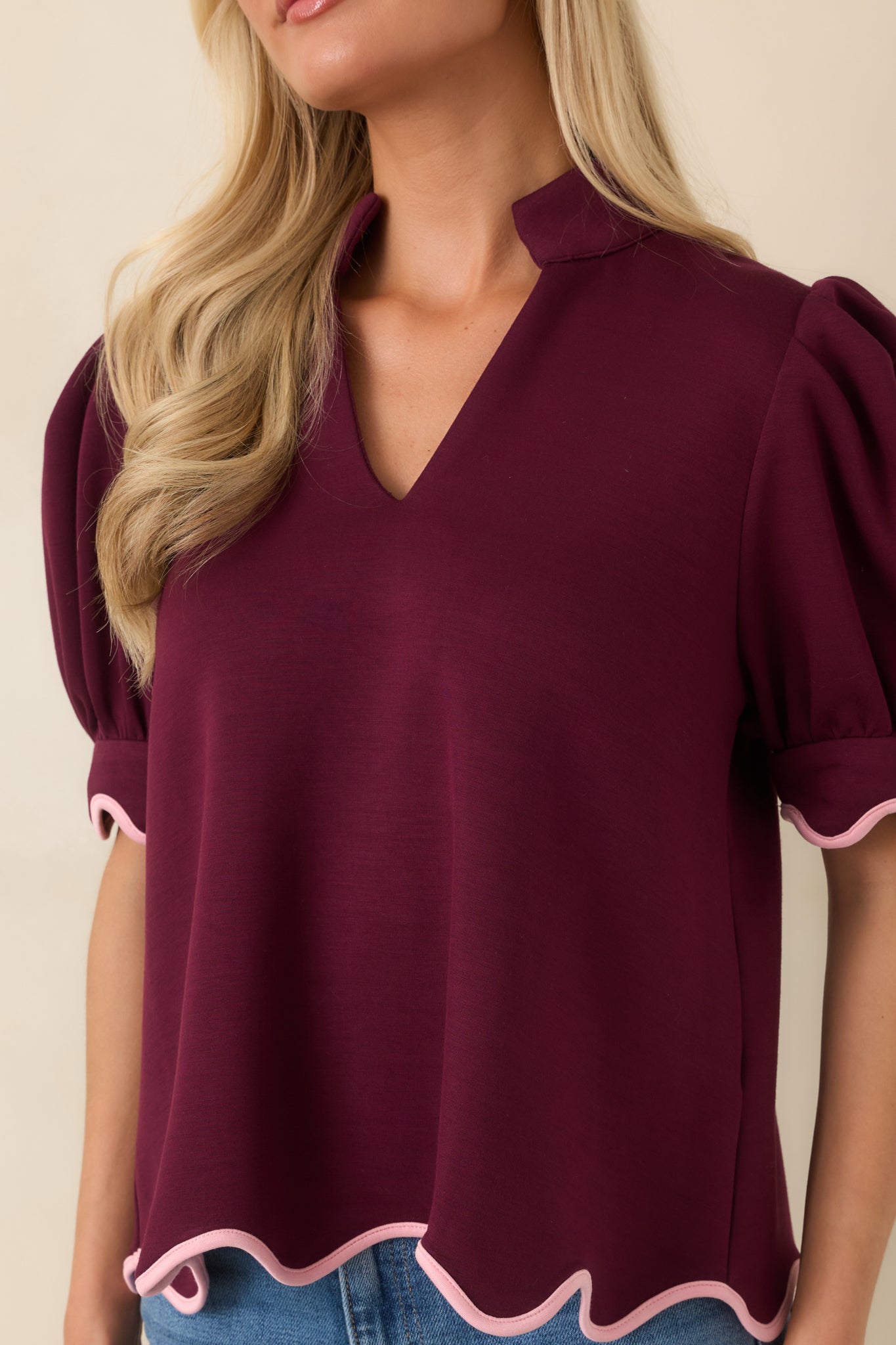 Close-up of the burgundy top showcasing the soft knit fabric, split neckline, and blush pink scalloped trim detailing.