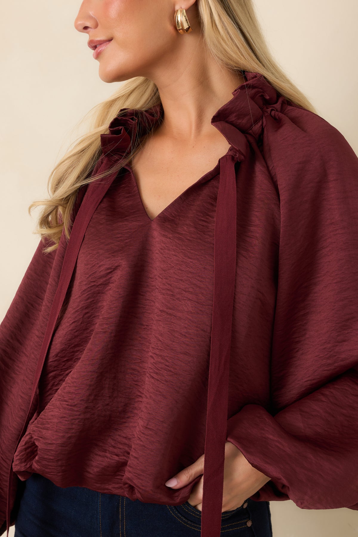 Close-up of the burgundy top’s ruffled stand collar, split V-neckline, and long ties against the crinkled fabric.