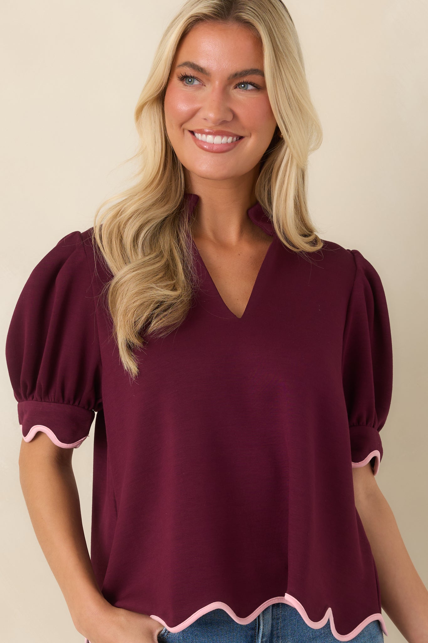 Detailed view of the burgundy top featuring blush pink scalloped trim along the sleeve cuffs and lower hem.