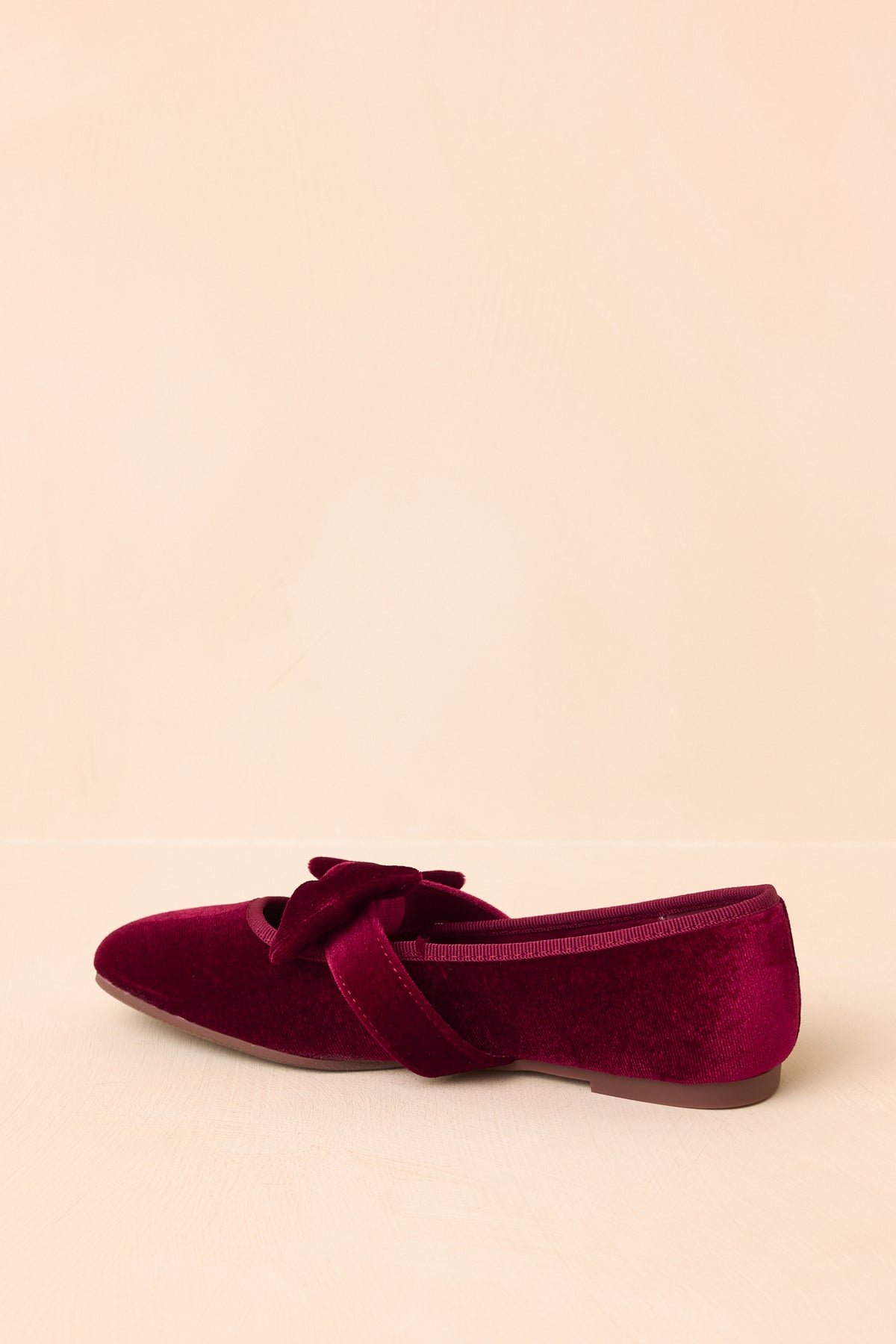 The bow-adorned Mary Jane strap adds a distinctive accent to the burgundy velvet design.
