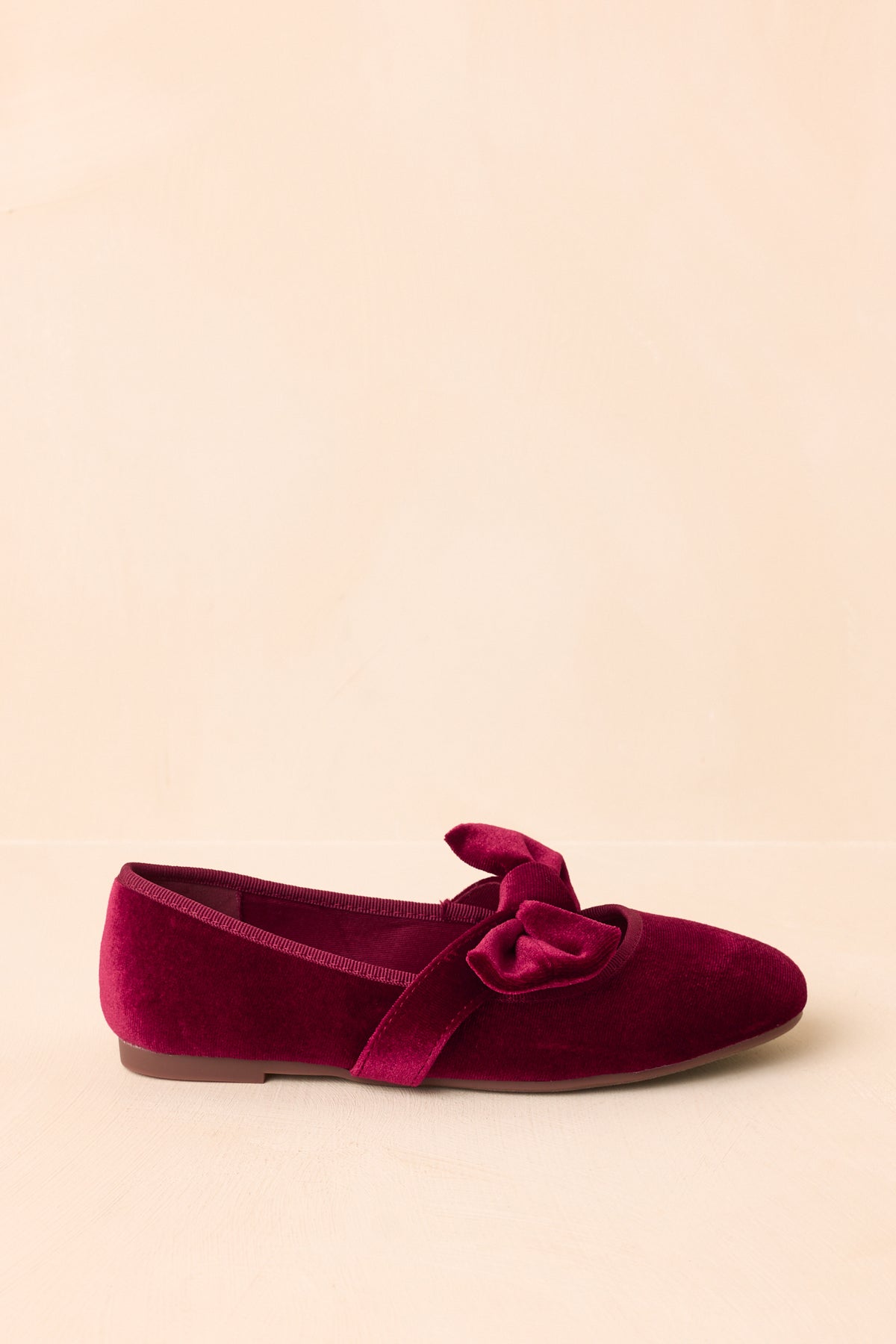 Burgundy velvet Mary Jane flats showcase a rounded toe and decorative bow across the strap.
