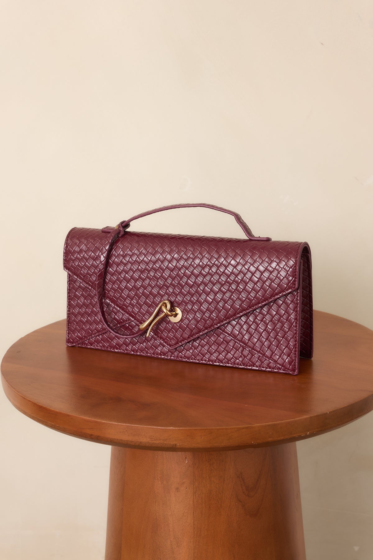 Burgundy clutch showcasing textured woven faux leather and sculptural gold-tone hardware.