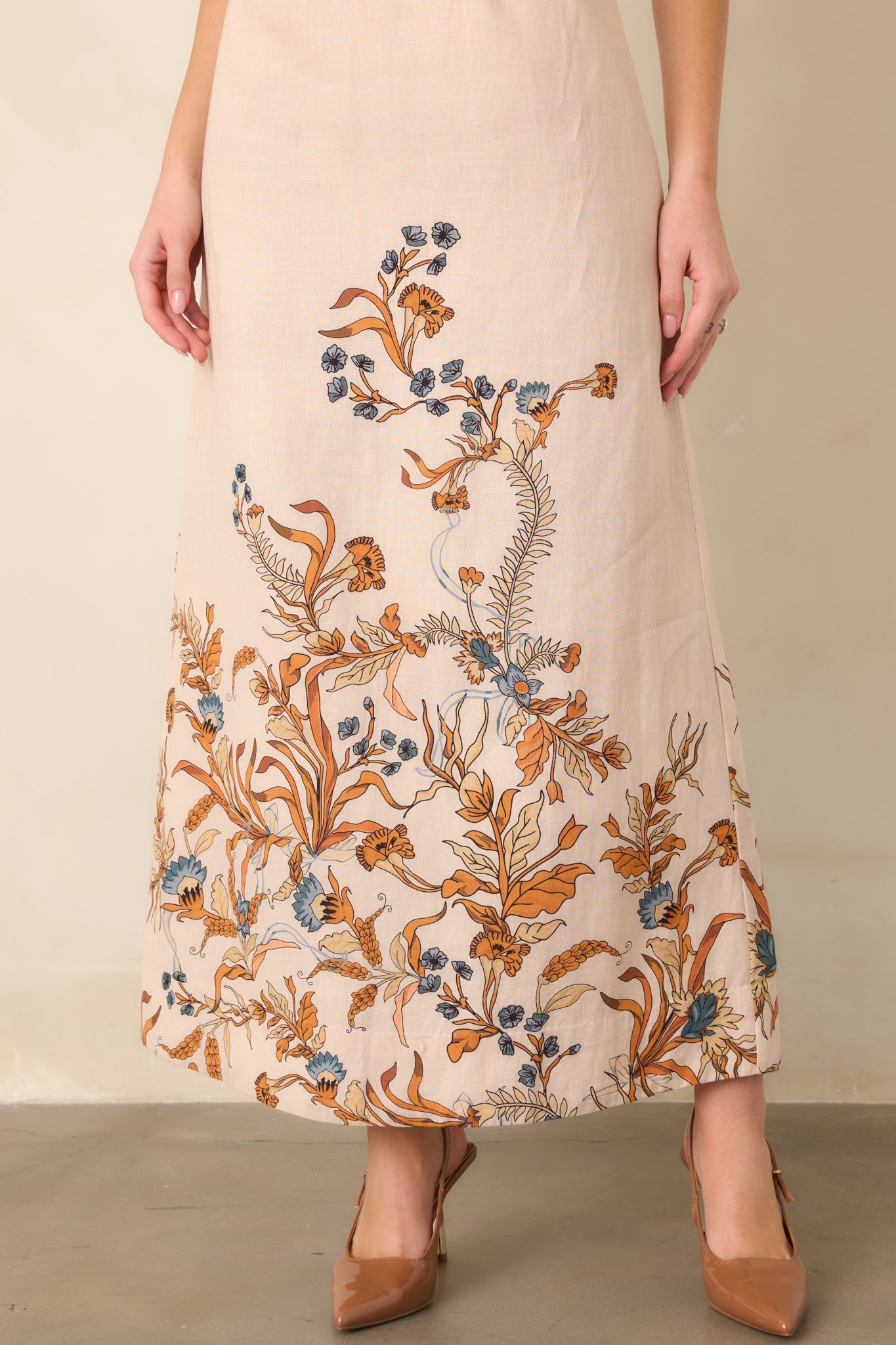 Burnt orange and muted blue floral accents decorate the lower hem of the long column-inspired skirt, adding a vibrant finishing detail.