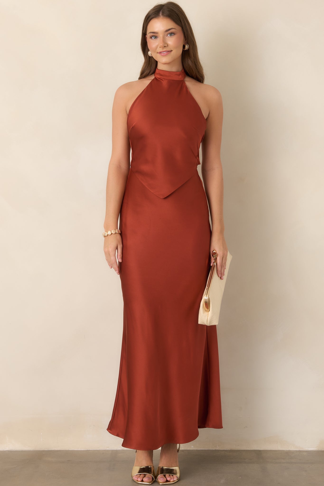 Fluid satin maxi dress in rich burnt sienna, showcasing the high halter neckline, defined pointed bodice, and flowing floor-length skirt.
