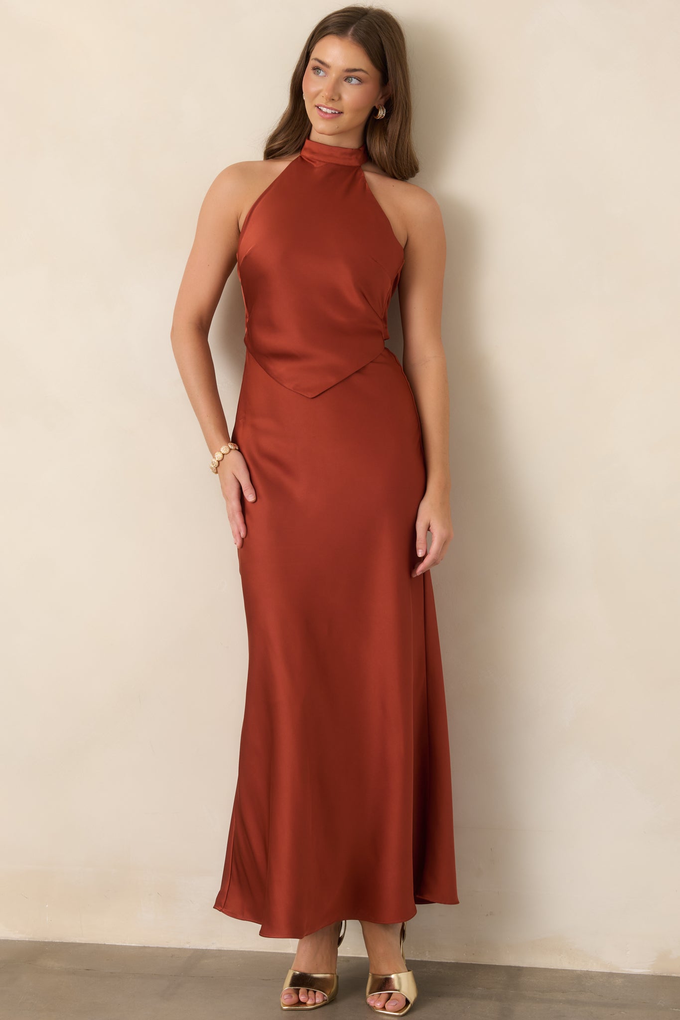 Burnt sienna satin maxi dress showcasing a sleek halter neckline, pointed bodice overlay, and fluid floor-length skirt with graceful movement.