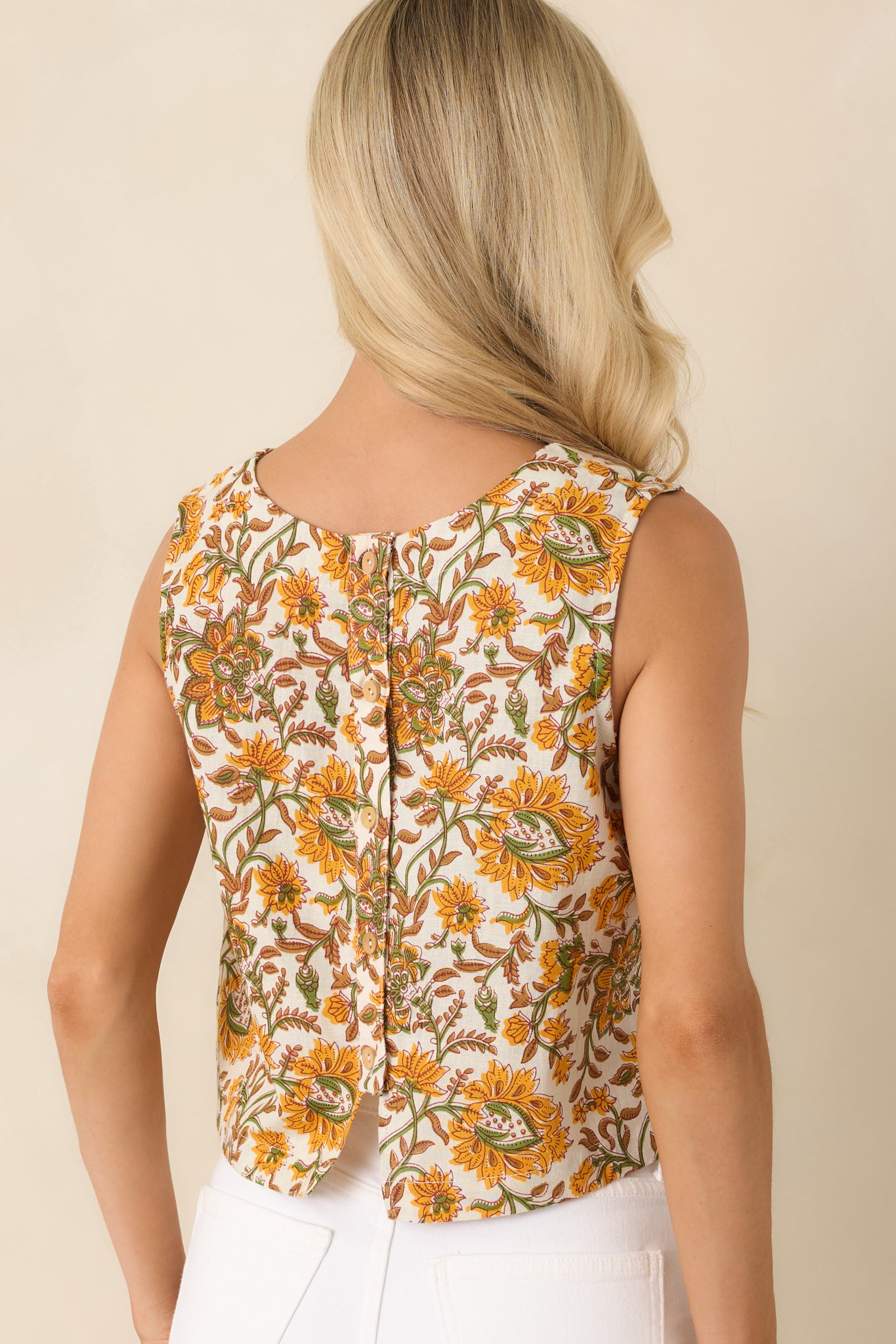 Rear view of the sleeveless cropped top featuring a full button-back placket and an allover marigold, olive, and tan floral print.
