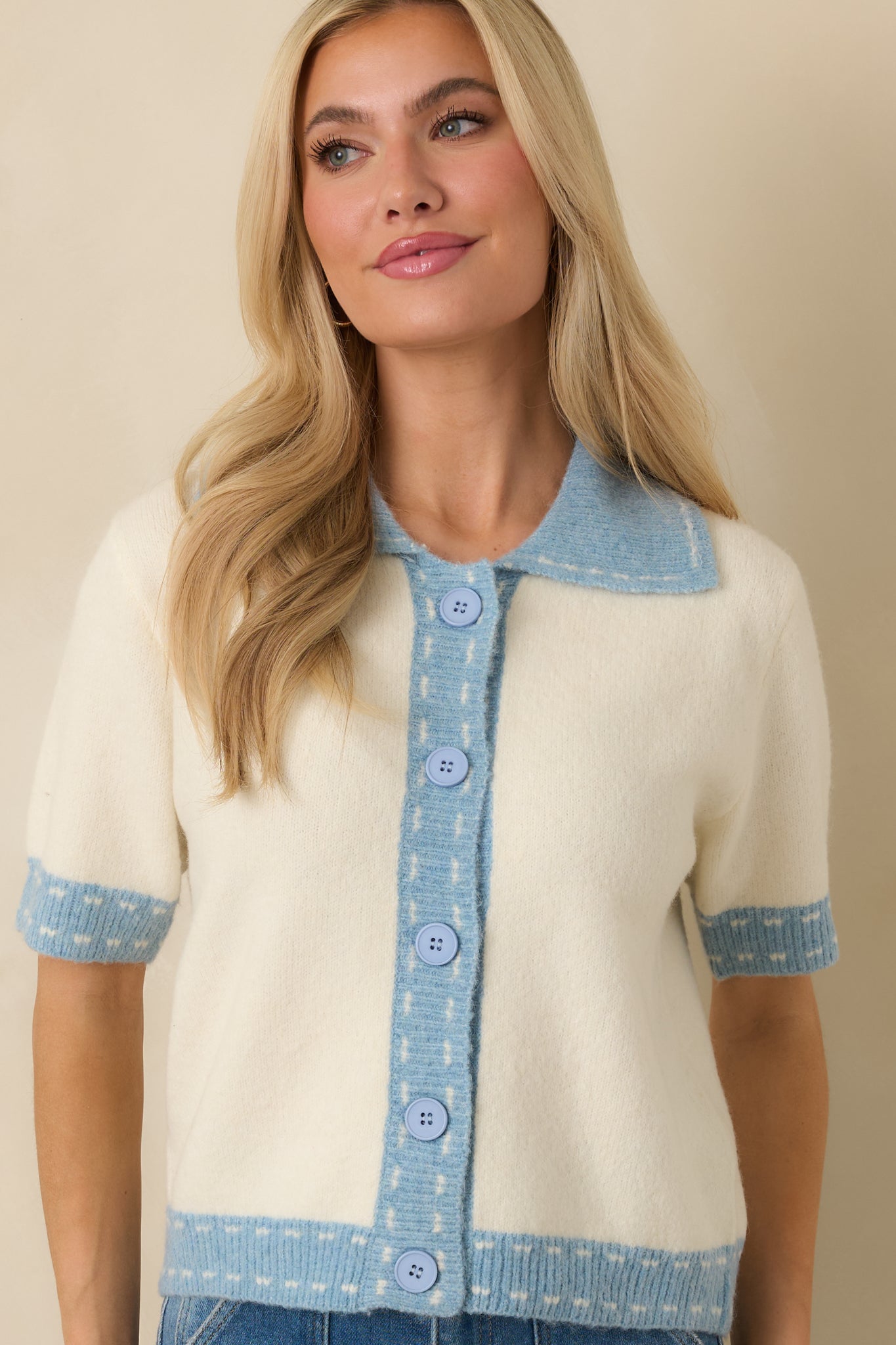 Button-front detail on ivory cardigan highlighted by tailored collar shaping and soft blue trim.