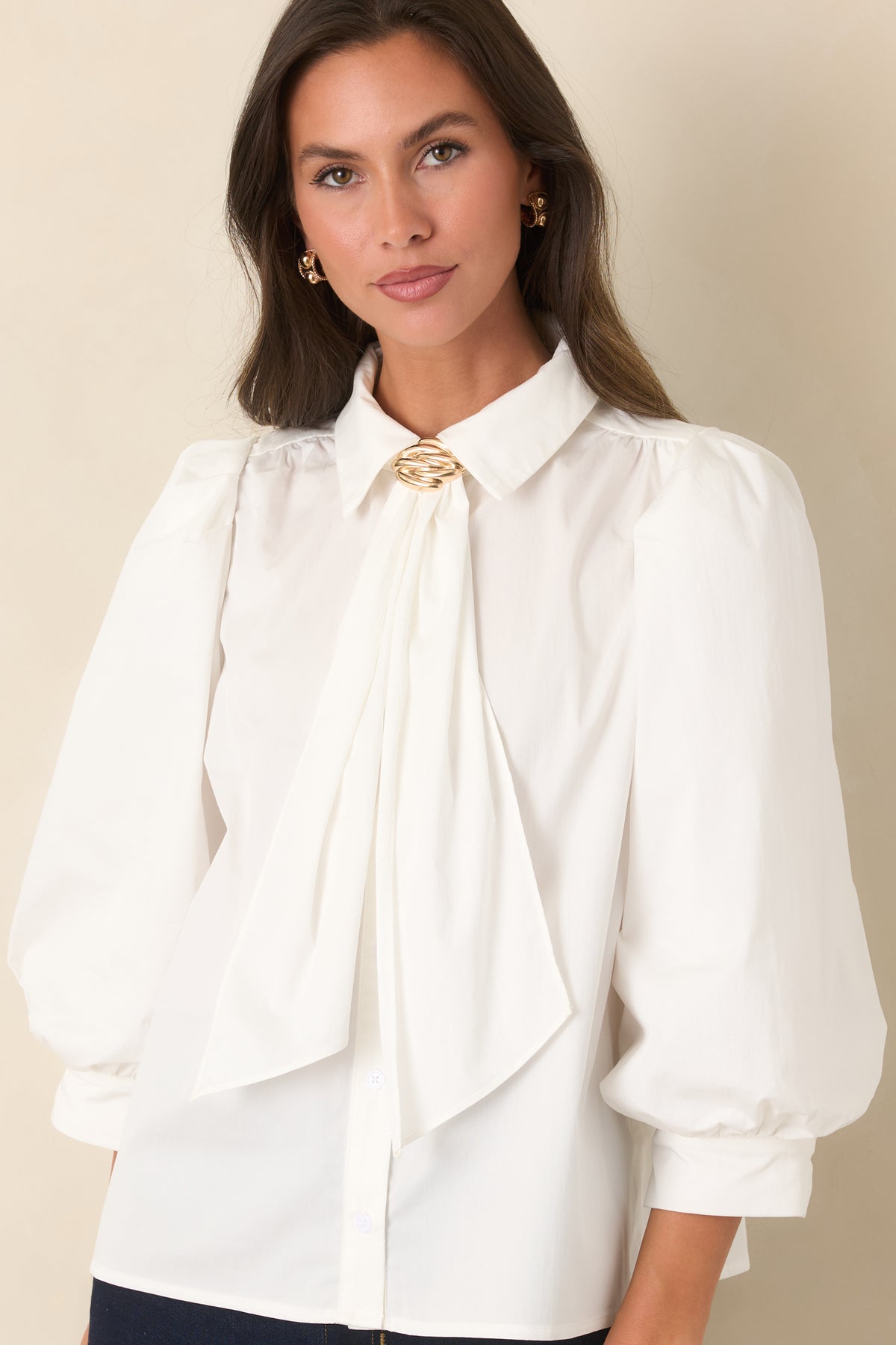 Button-front blouse highlighting the pointed collar, draped neck ties, and sculptural gold-tone accent.
