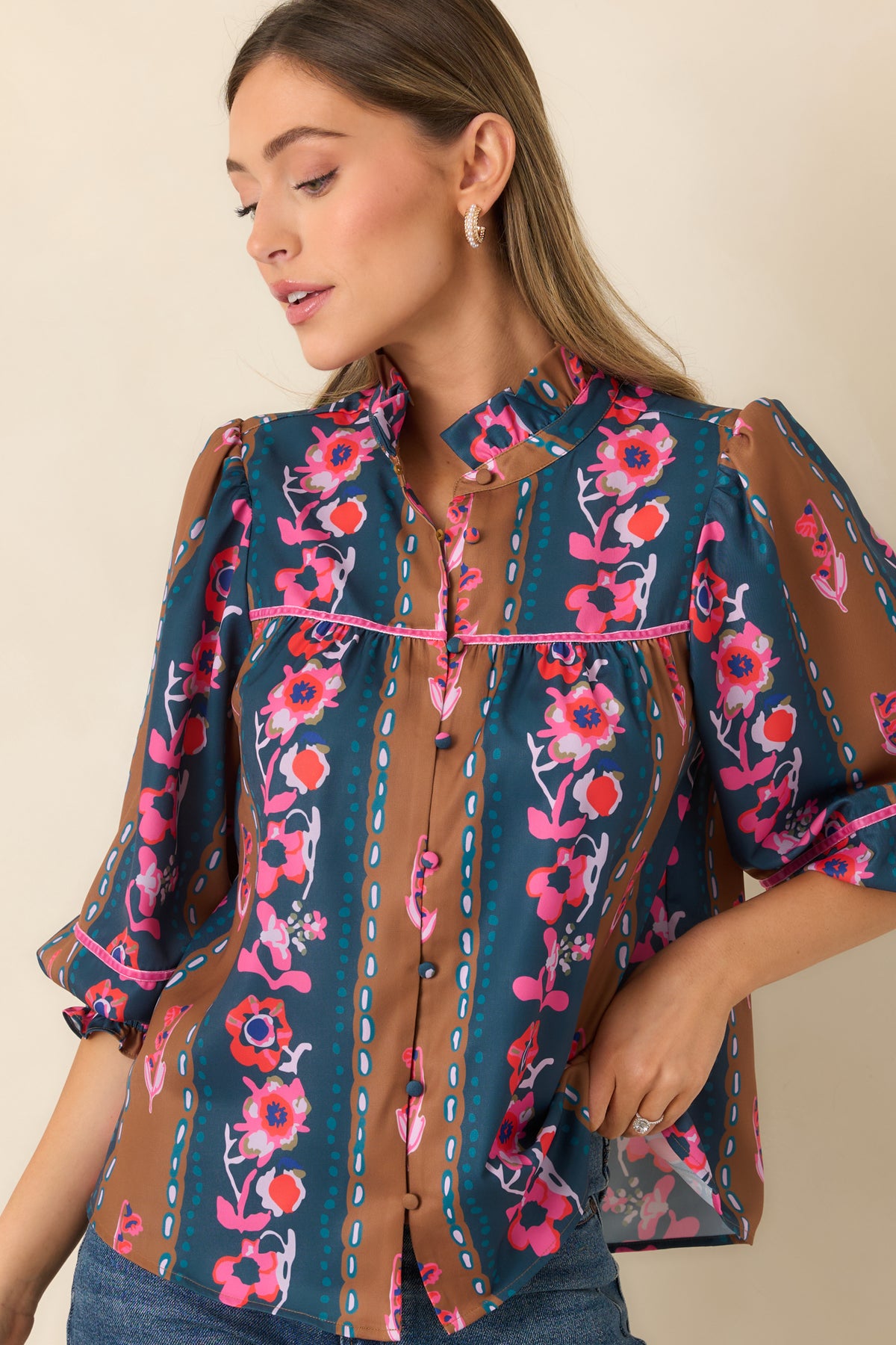 Pink, coral, and ivory blossoms decorate the striped blouse alongside warm caramel and deep teal bands.