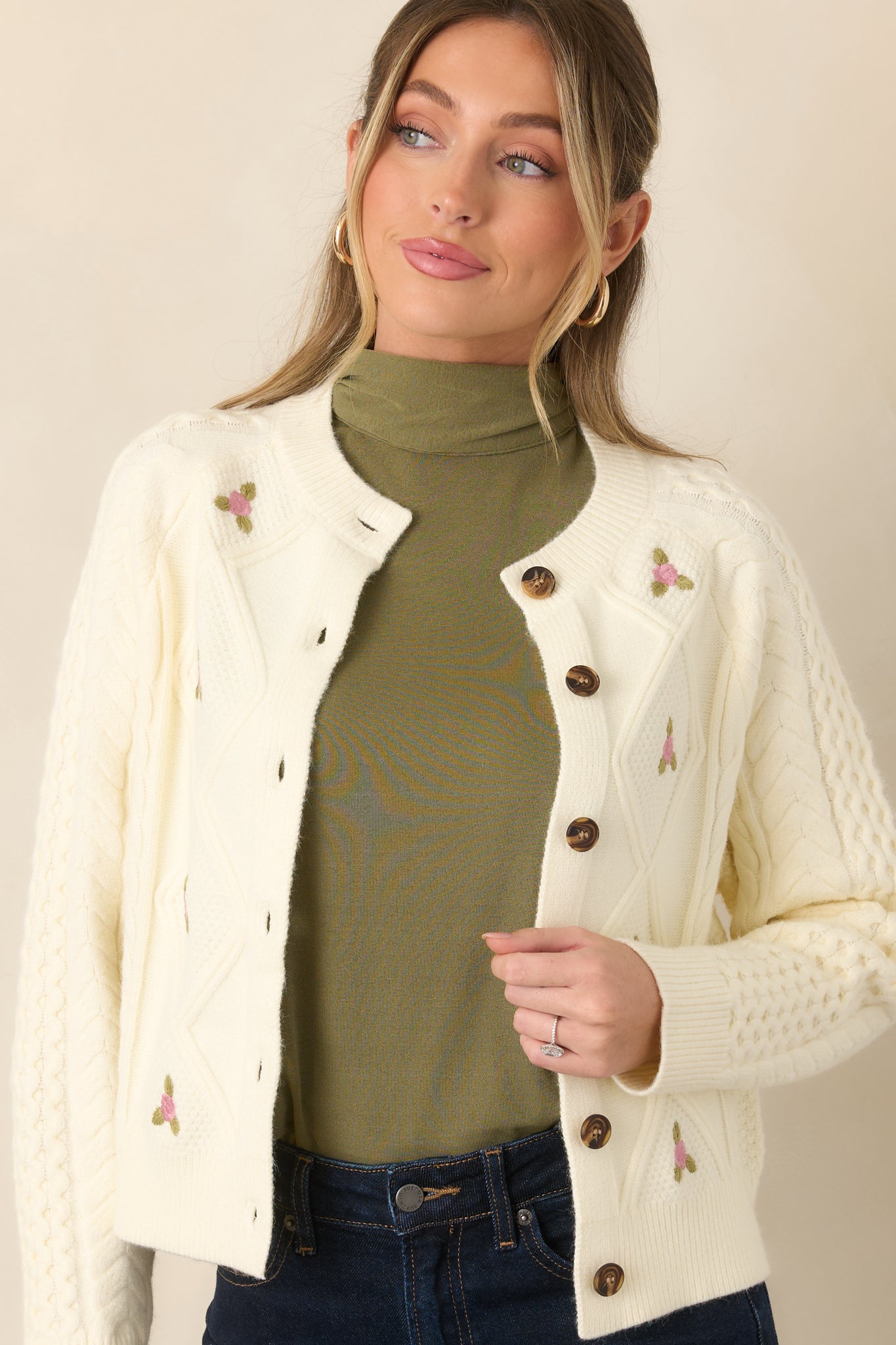Close view of the cardigan highlighting intricate cable-knit texture, pink floral embroidery, and tortoise-style button closures.